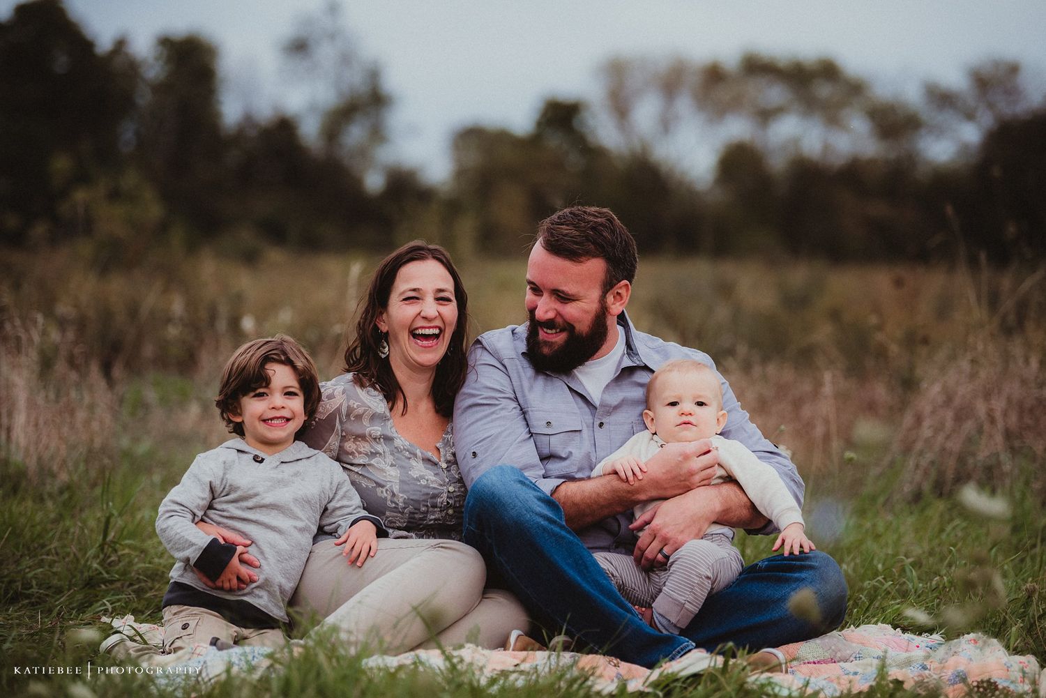 Candid family portrait on blanket in rustic field setting.