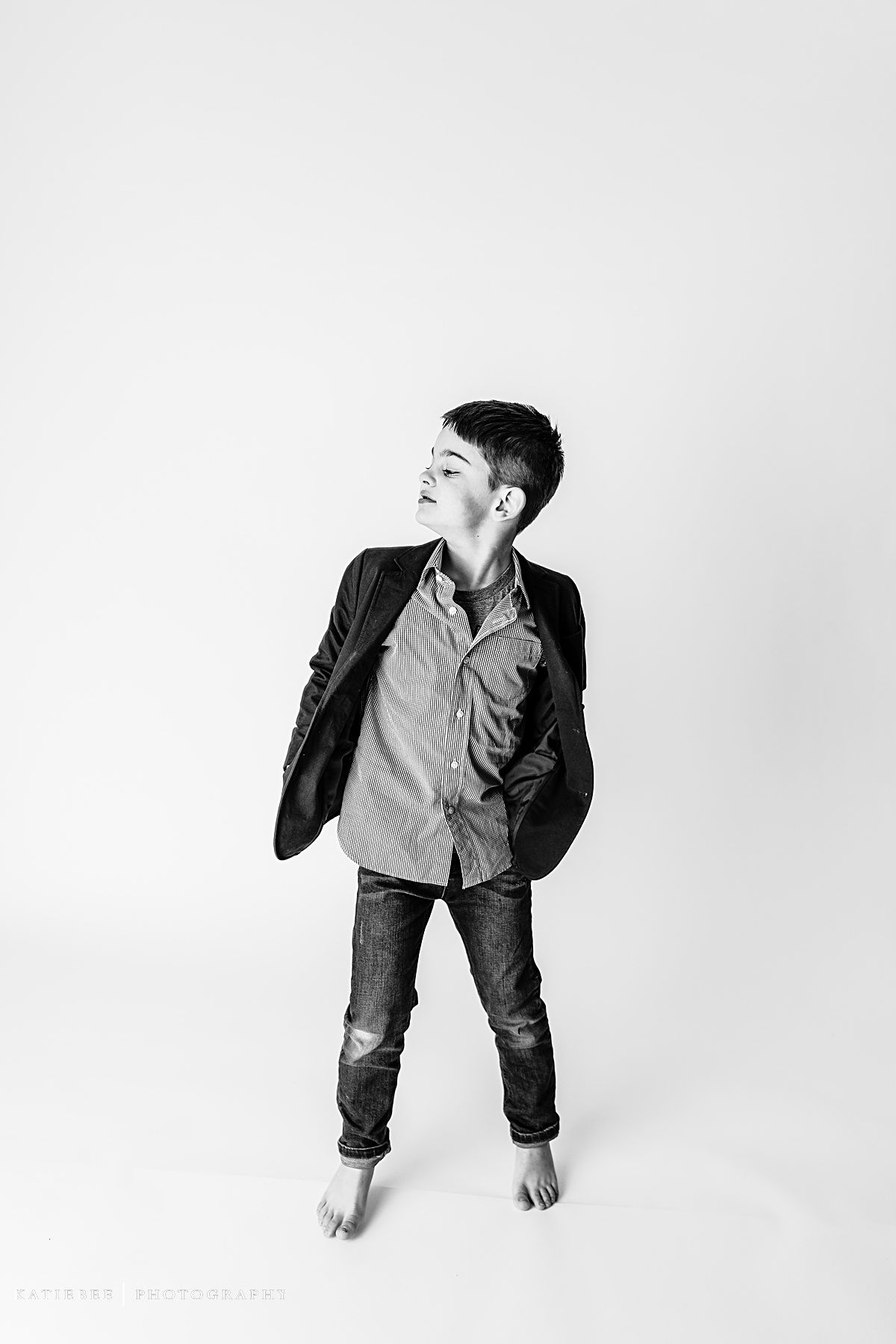 Child in striped shirt and jacket striking dynamic pose in black and white studio shot.