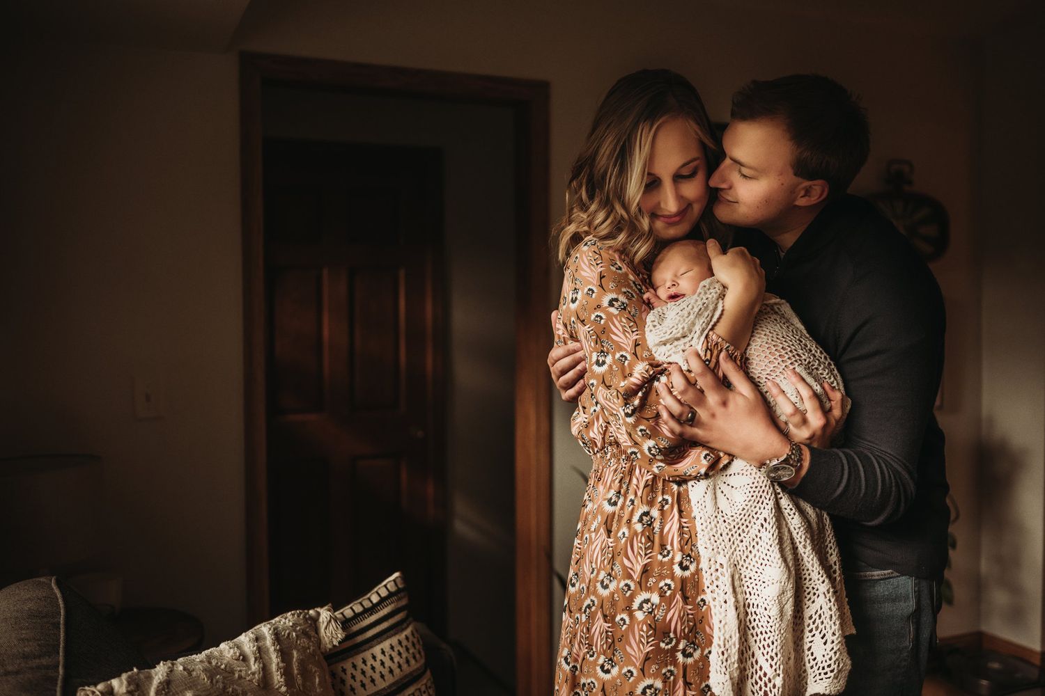 An intimate family portrait showing affectionate parents embracing while holding their newborn.