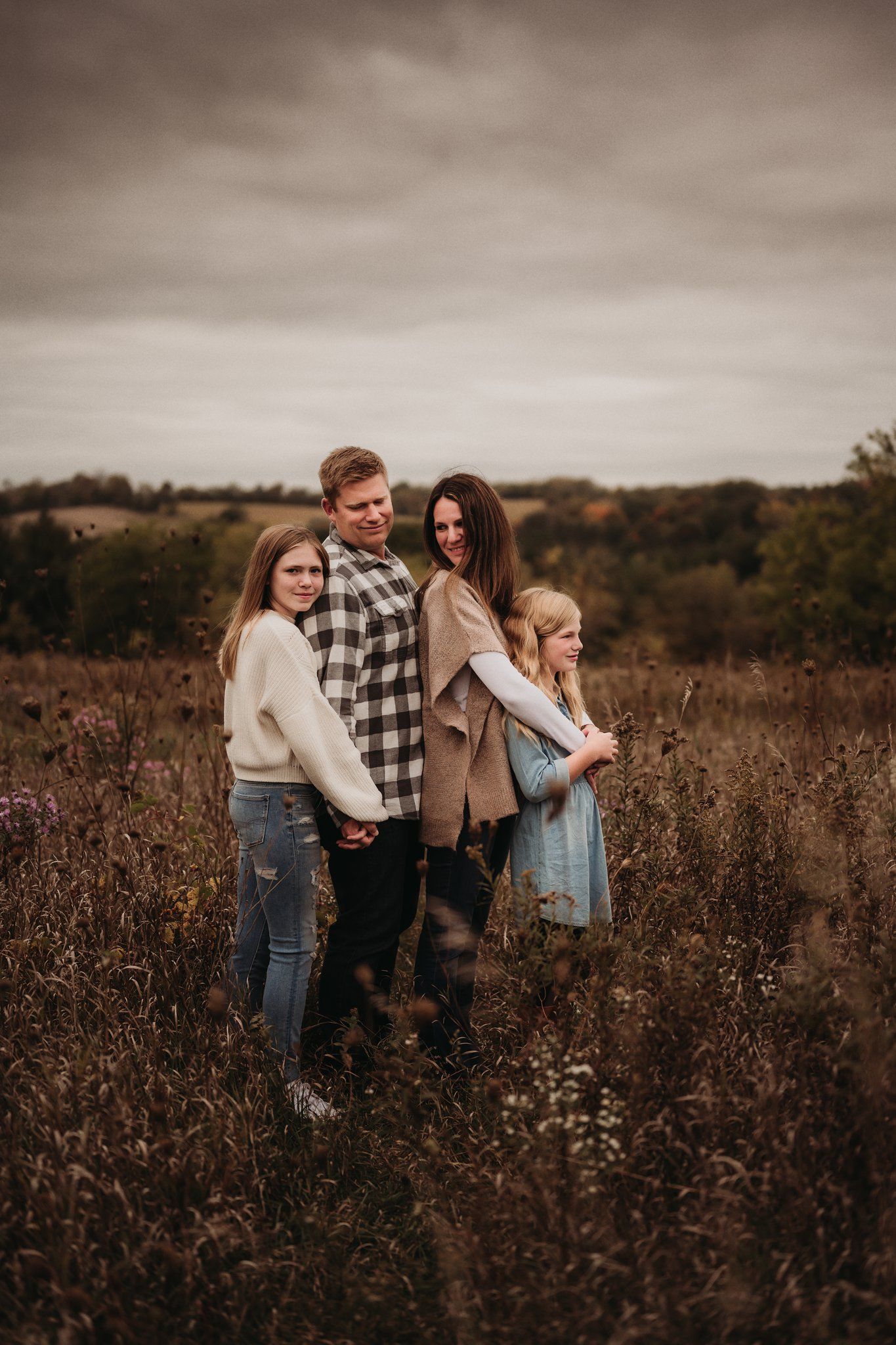 Family of four poses together in autumn field during golden hour.