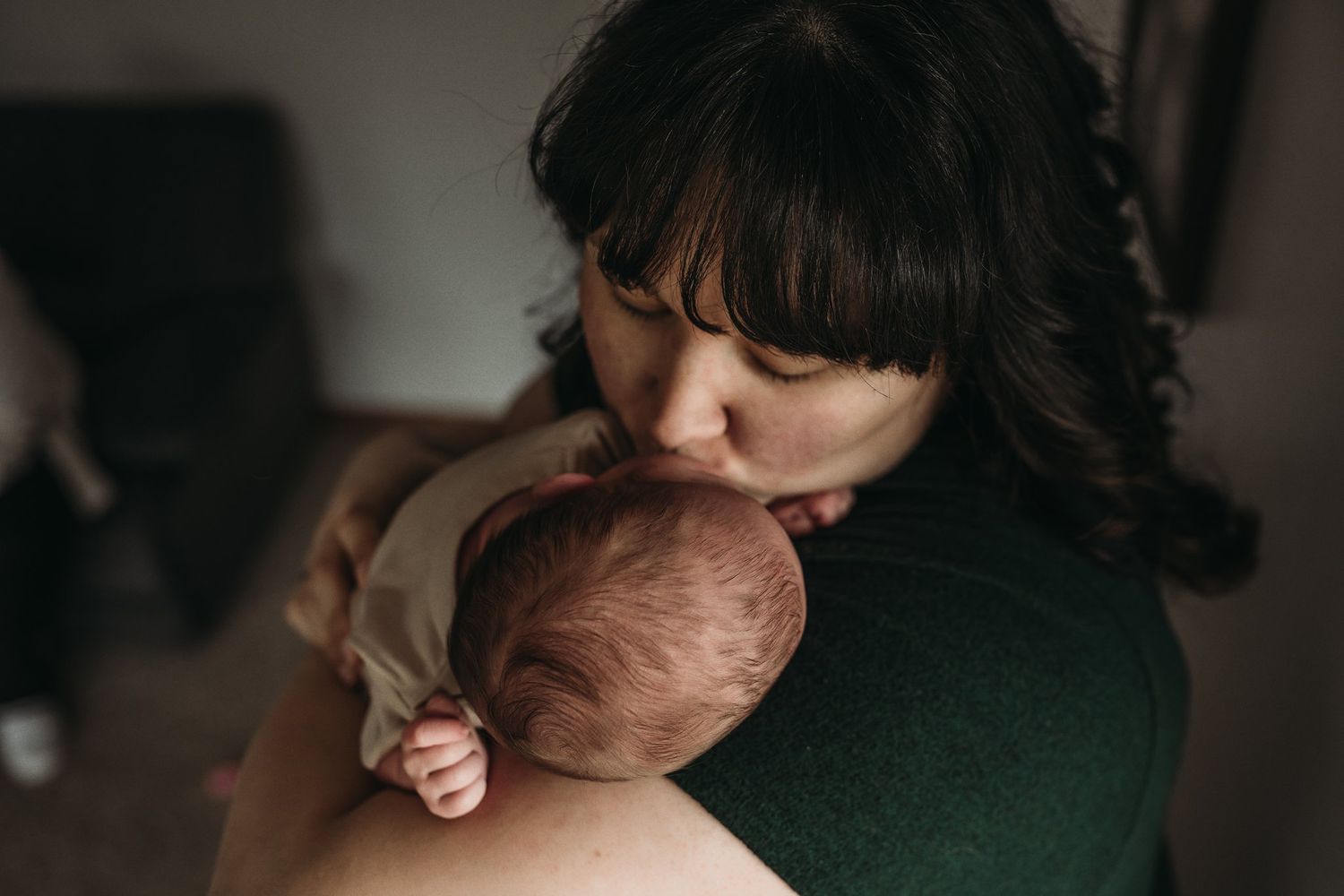 Intimate moment of gentle affection with a newborn baby in dark green clothing.