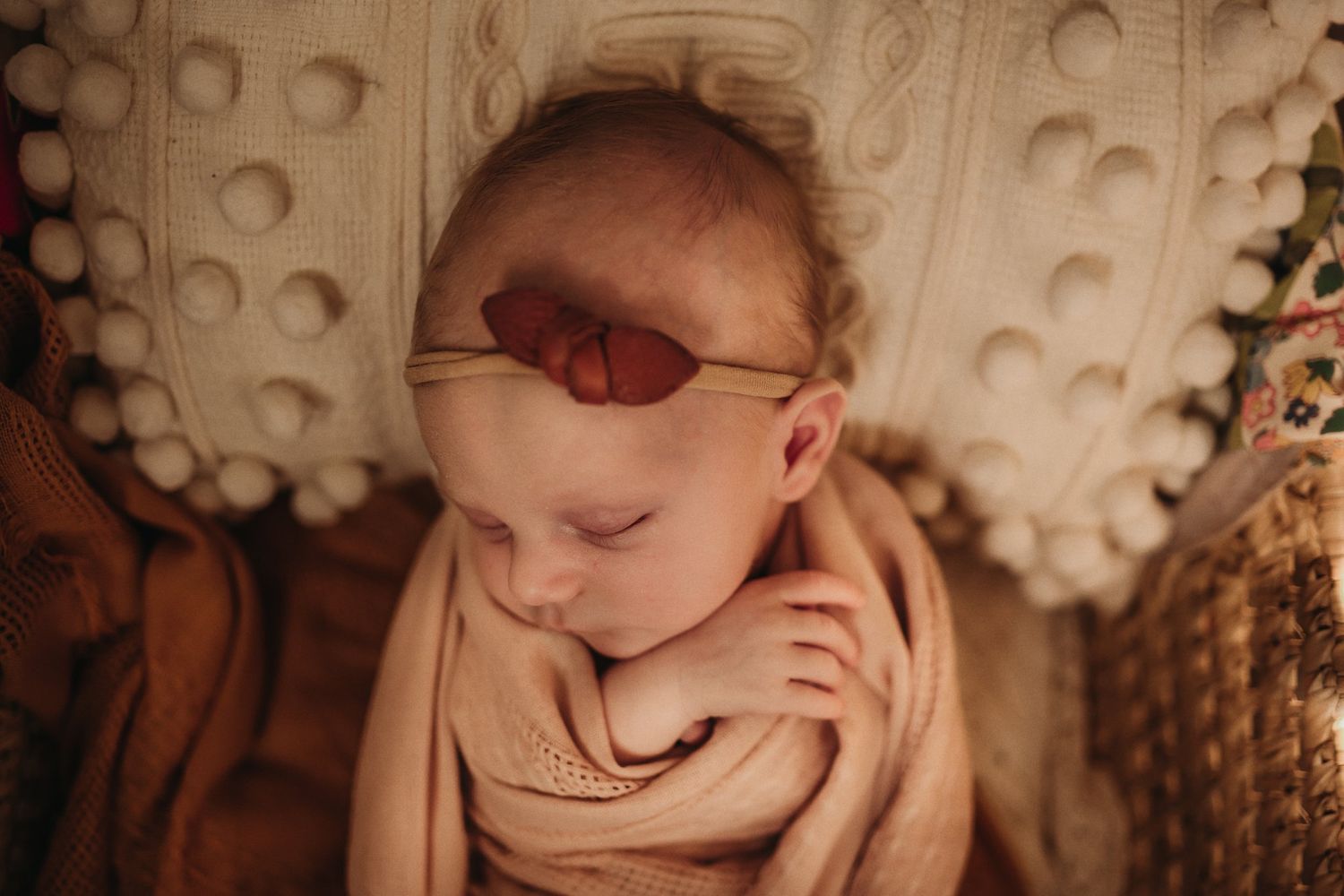 Close-up of a sleeping baby wearing a headband and wrapped in neutral colored fabric.