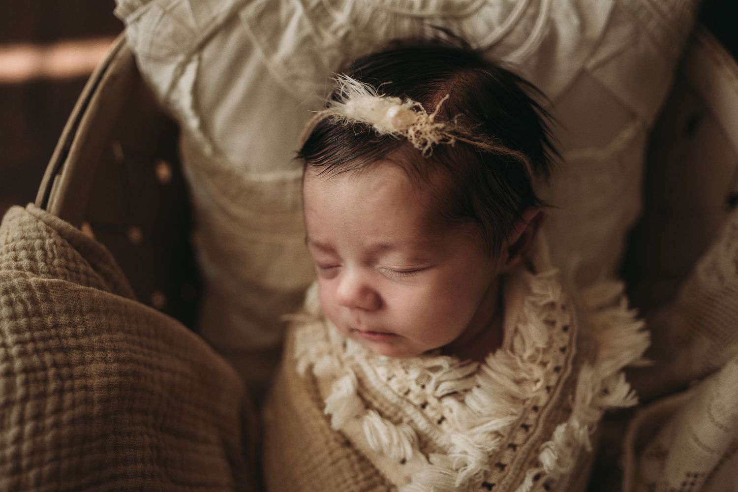 Sleeping baby wearing a delicate lace headband nestled in soft cream pillows.