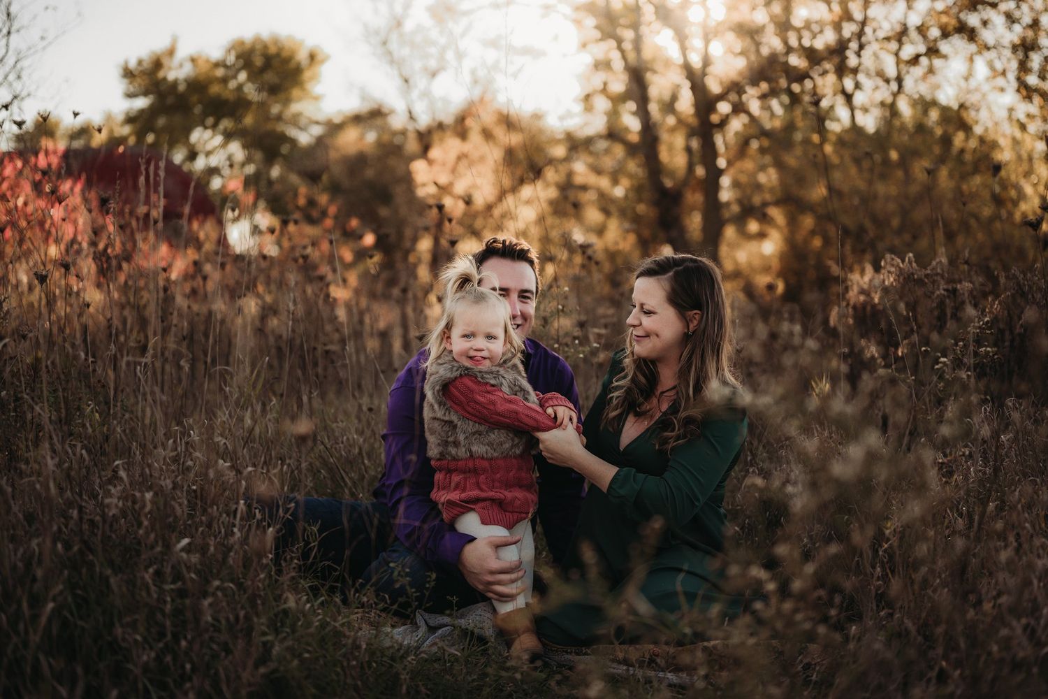 Family enjoying playful moment together in autumn field at sunset.