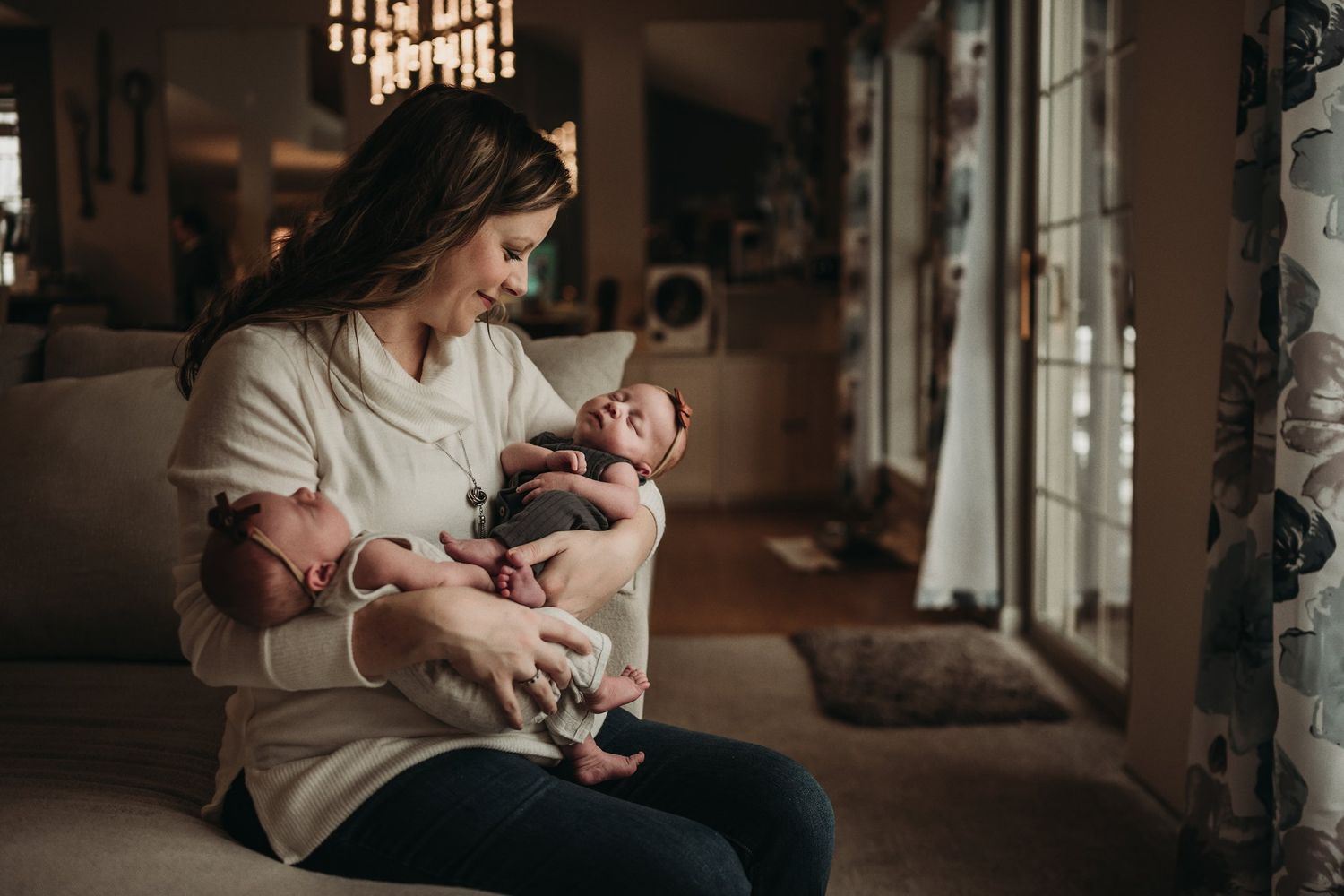 Intimate moment captured in natural light as parent cradles infant by large windows.