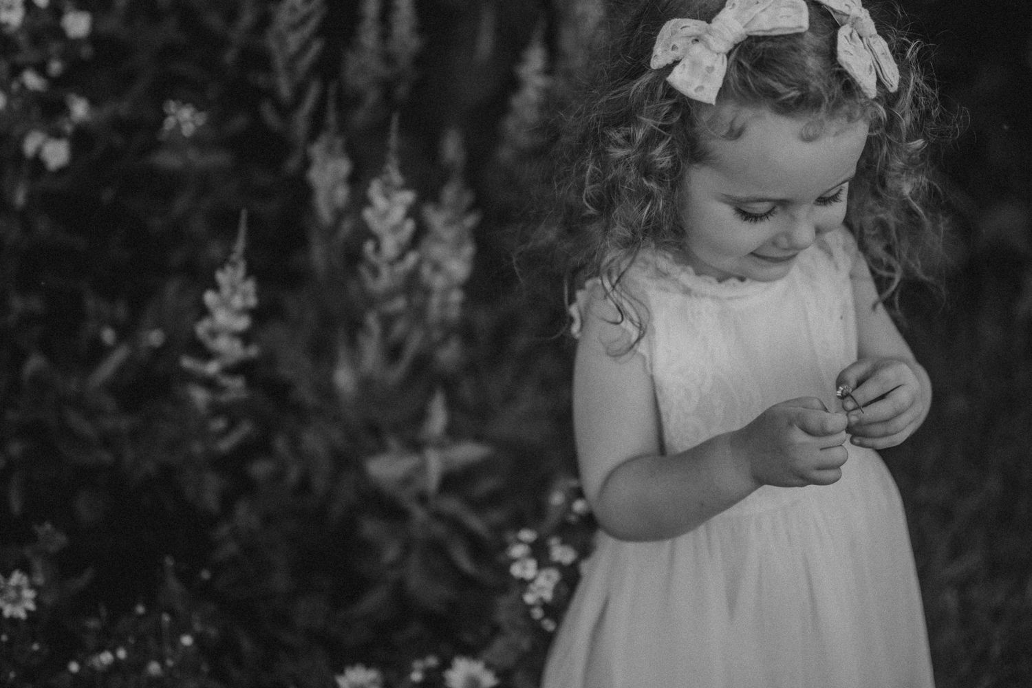 Black and white photo captures a tender moment among garden flowers and natural light.