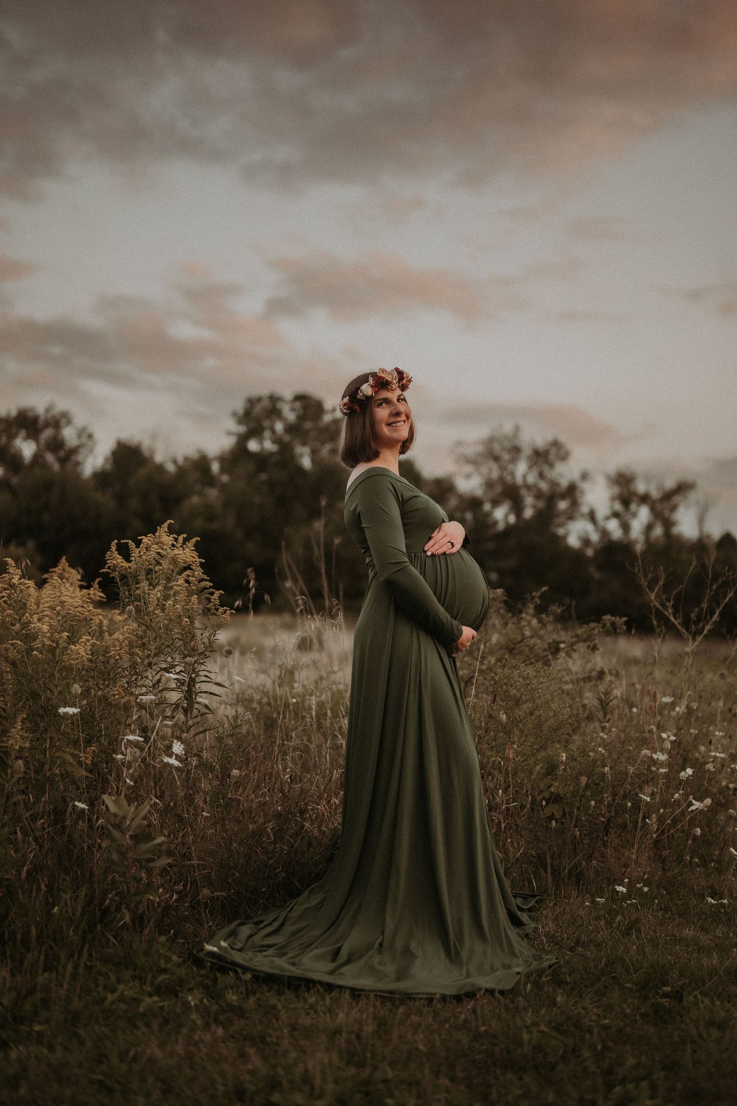 Graceful maternity silhouette in flowing green dress during golden hour.