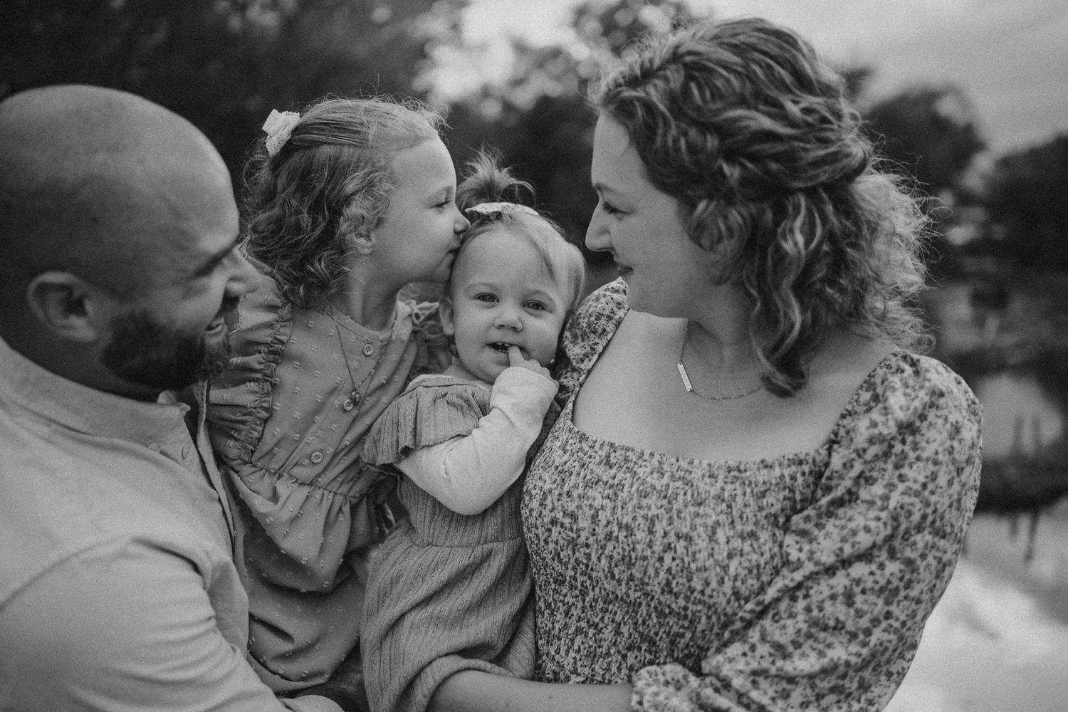 A heartwarming black and white family portrait showing loving interactions outdoors at sunset.