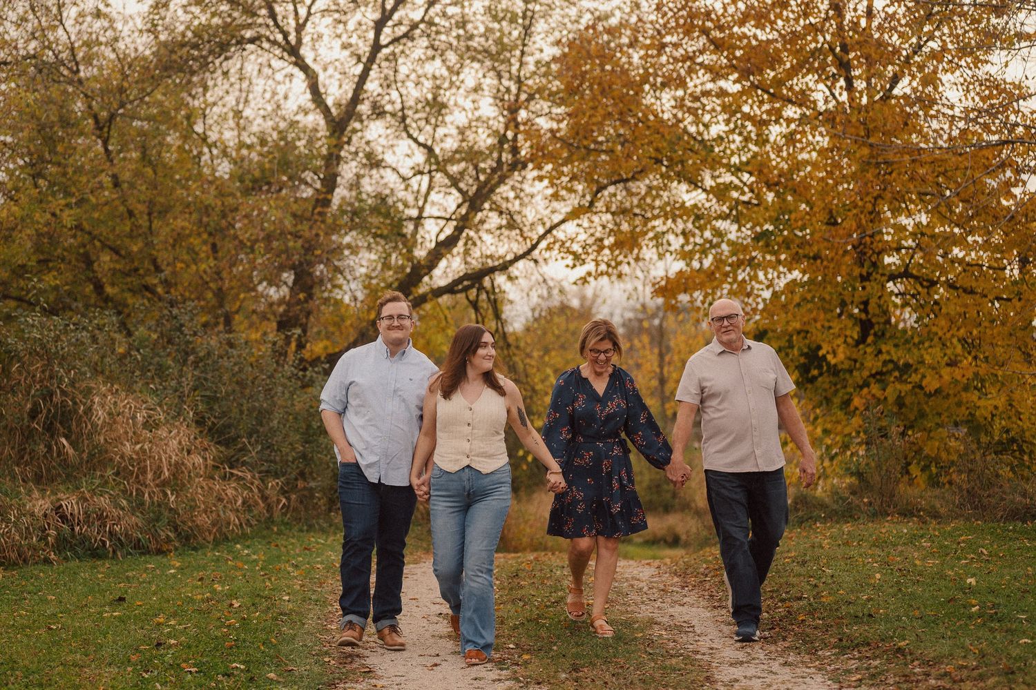 A group walks along a scenic autumn path with golden trees and fallen leaves during sunset.