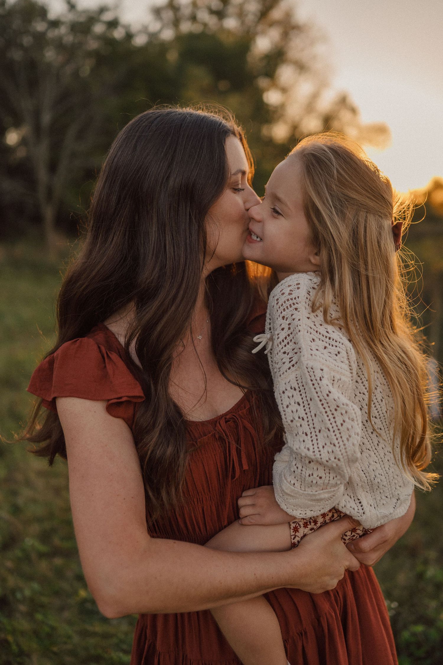 Tender moment captured between two people embracing in a field at sunset with golden backlighting.
