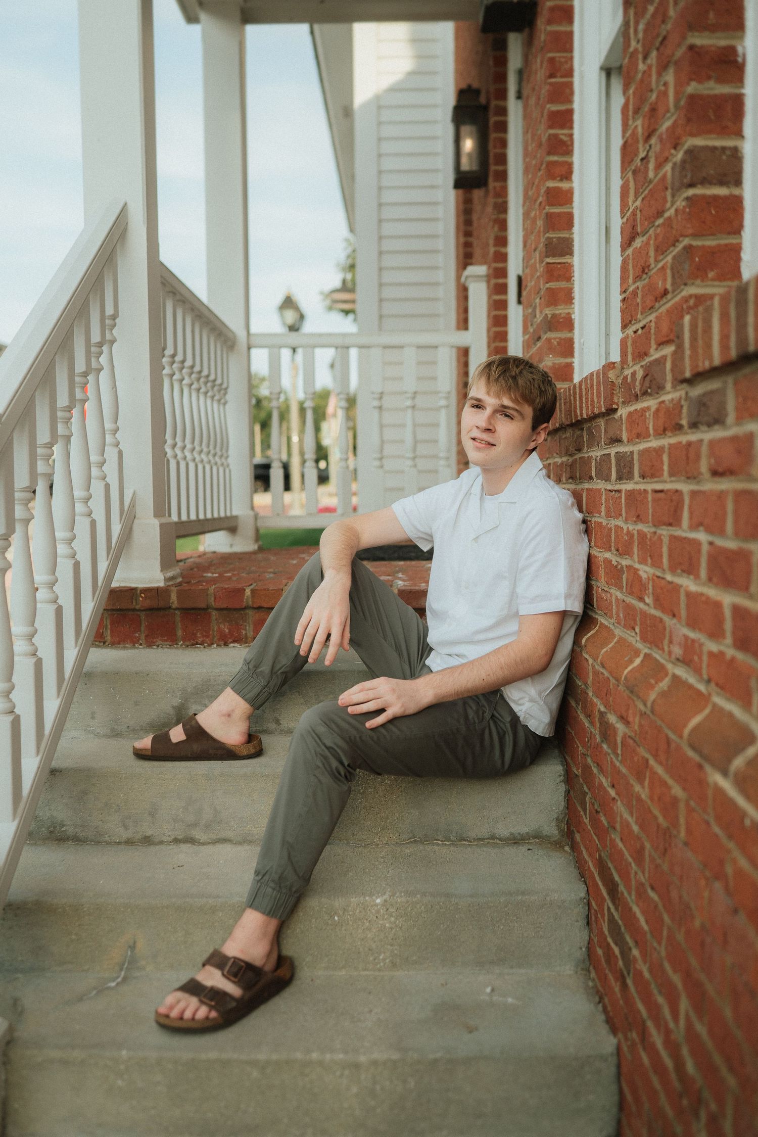Four sequential shots of someone lounging on concrete steps against a brick wall wearing sandals.