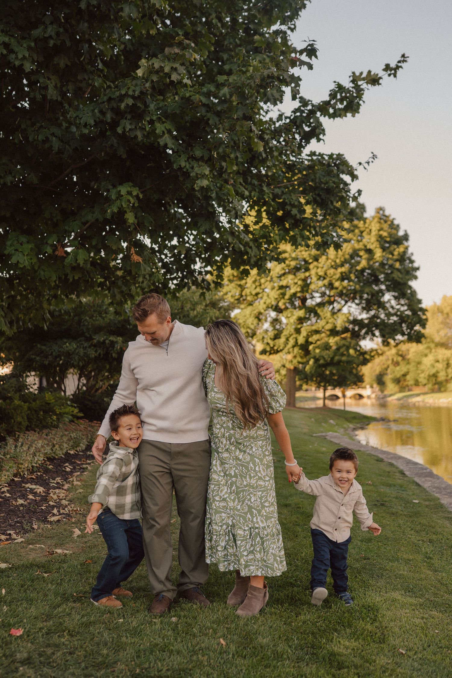 A family shares a playful moment together on a grassy path beside a tranquil lake during golden hour.