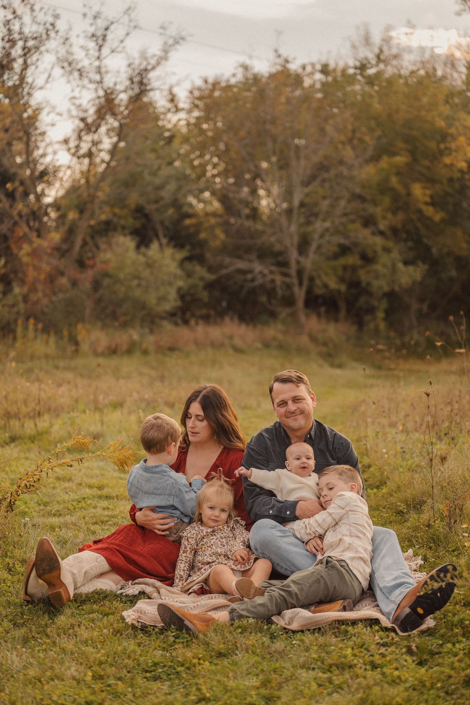 Family relaxing together on blanket in field during autumn sunset photography session.