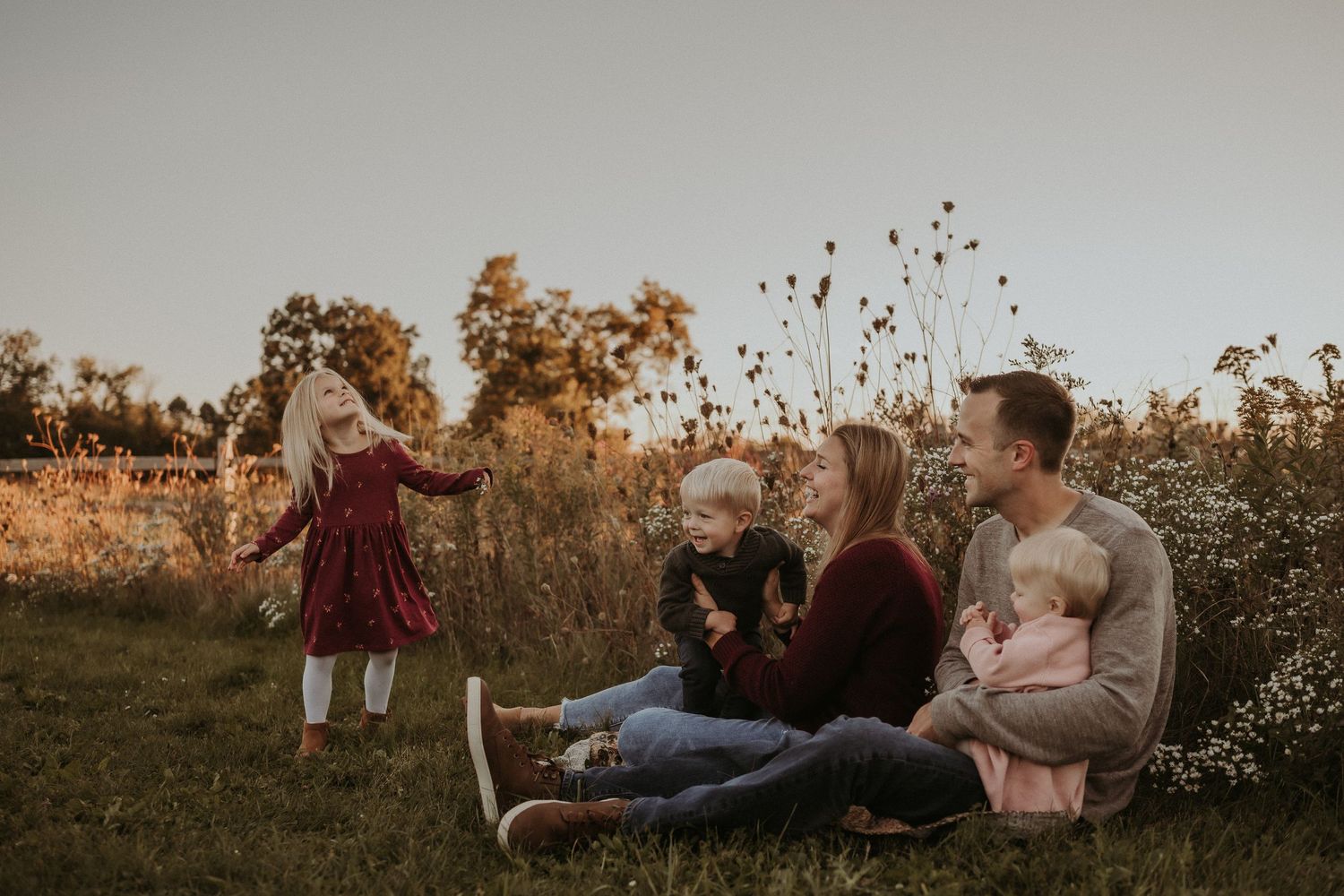 Playful outdoor family portrait session in a rustic field with wildflowers at golden hour.