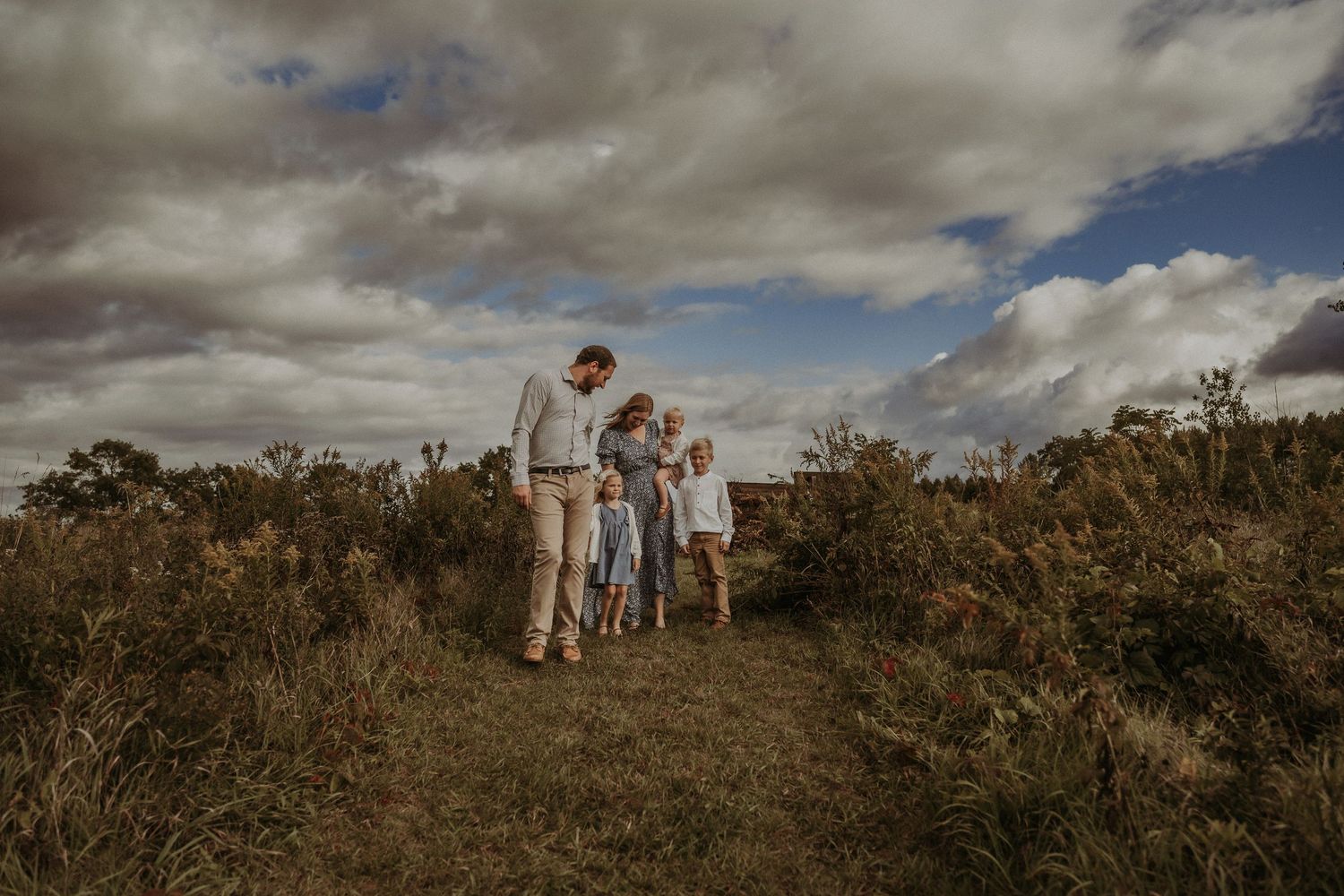 Intimate family portrait on a hiking trail surrounded by autumn brush and dramatic clouds.