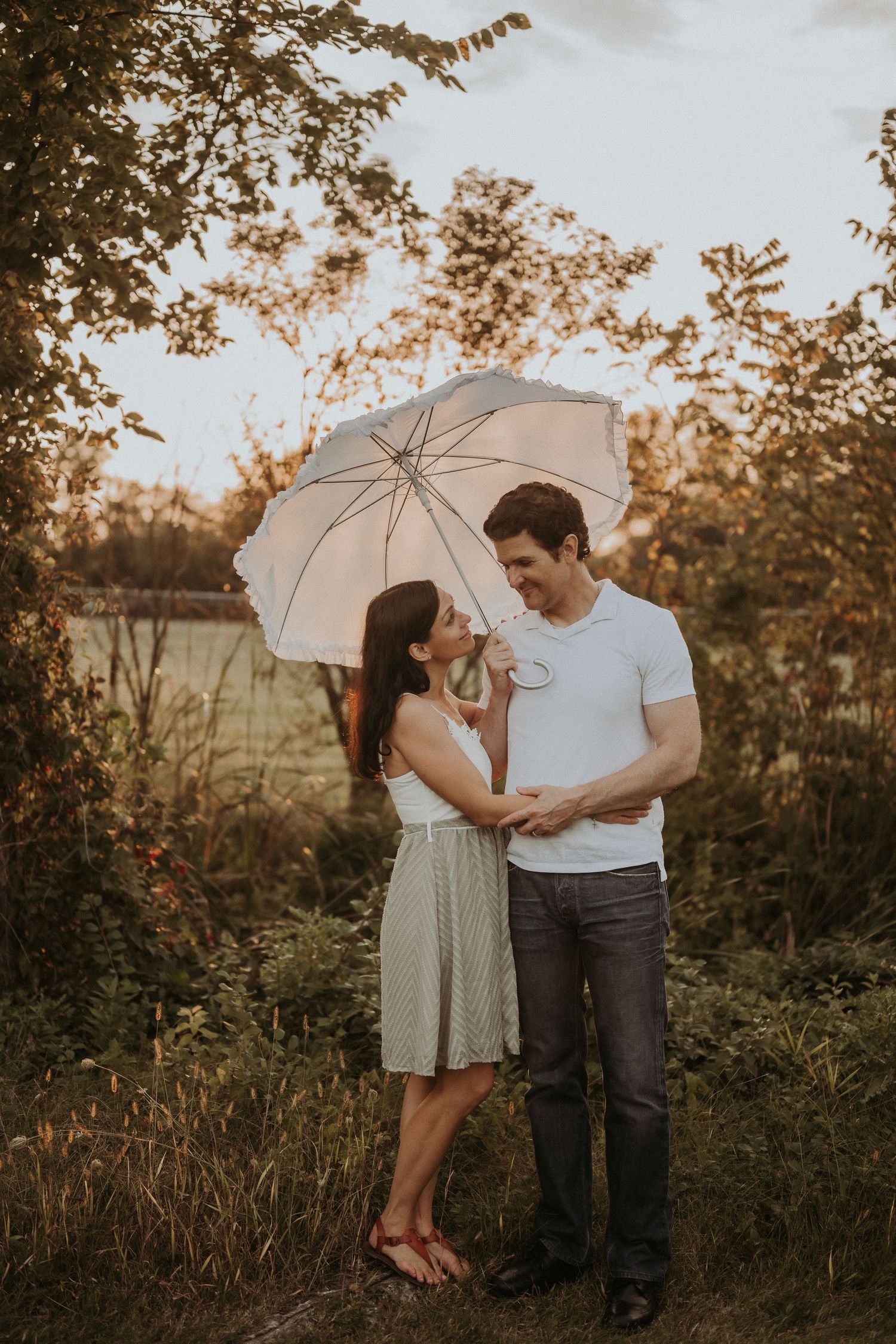 A couple shares a romantic moment under a white umbrella during golden hour.