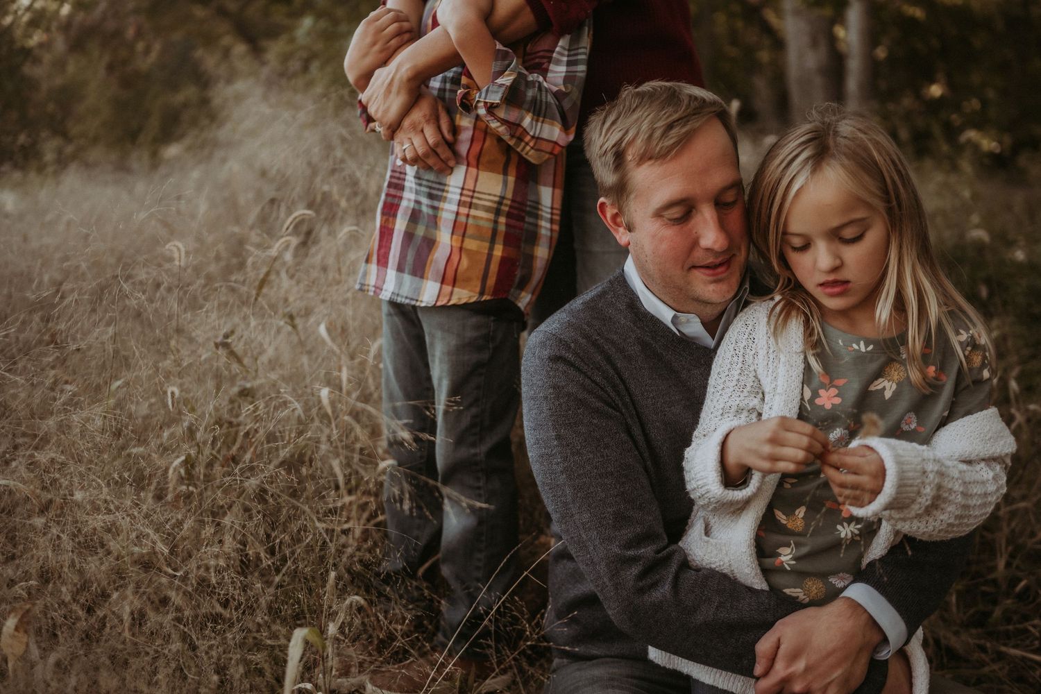 A sweet family portrait outdoors showing tender moments together in fall clothing against dried grass.