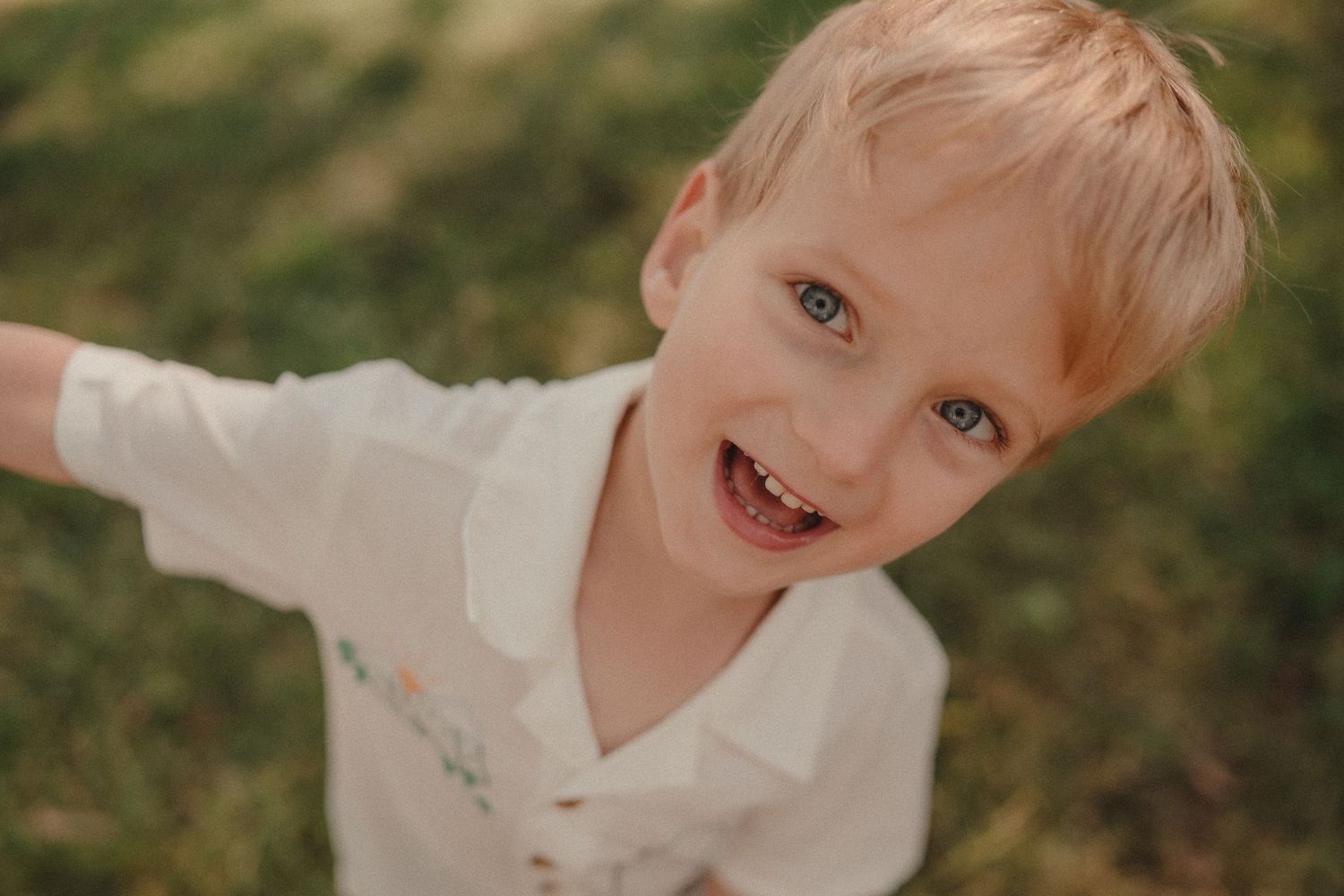 Happy young blonde boy with blue eyes smiling outdoors in natural light.