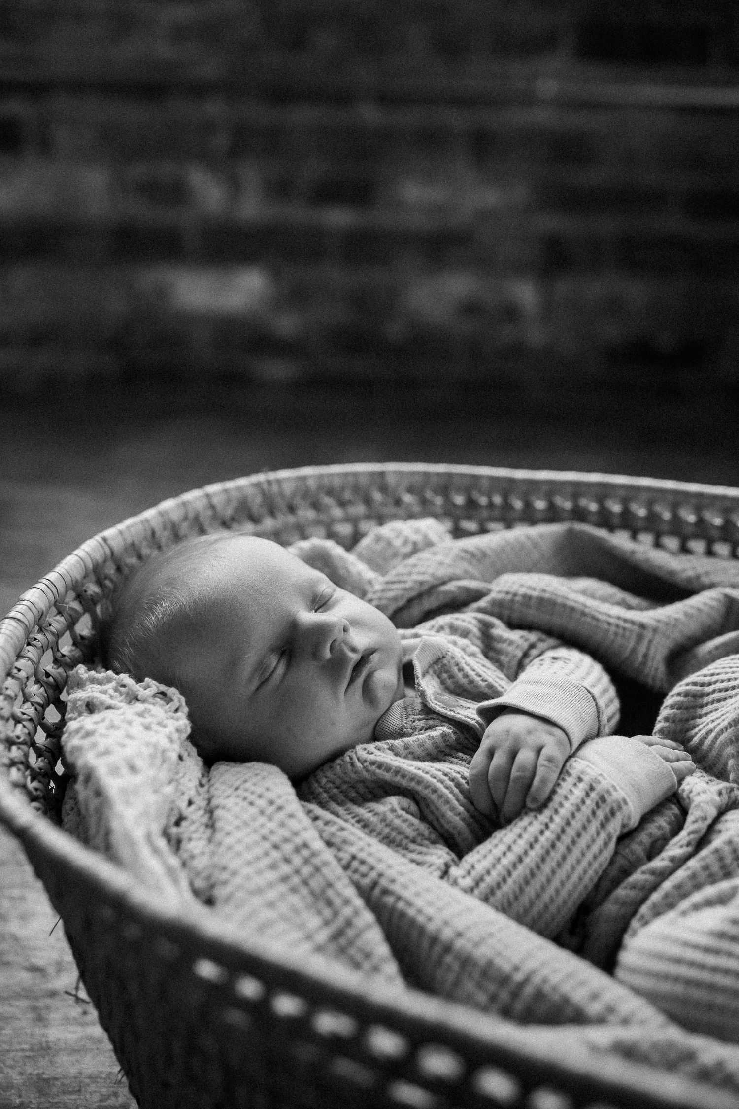 Peaceful newborn baby sleeping in a wicker bassinet wrapped in soft textured blankets.