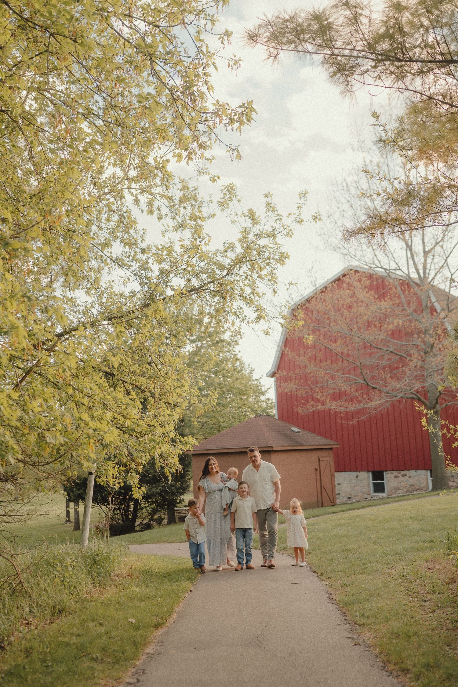 A happy family of five walks along a path with a red barn and autumn trees in the background.