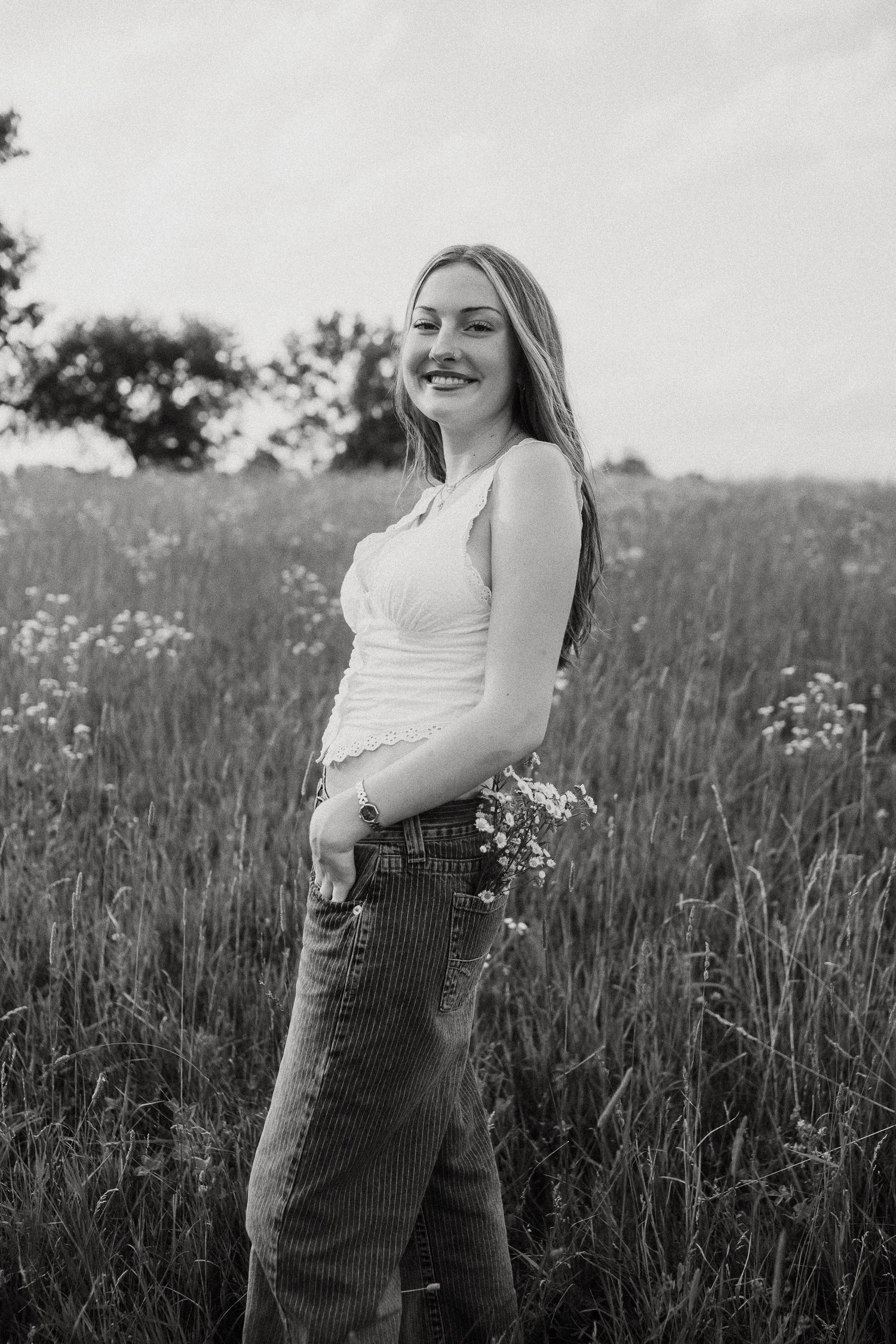 Black and white portrait of smiling young woman holding wildflowers in a meadow field.