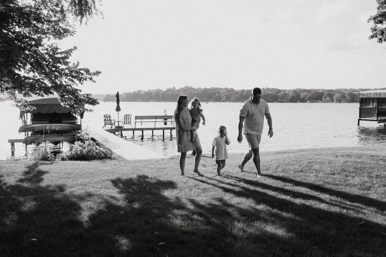 Black and white photo of a family walking along a lakeside dock on a sunny day.