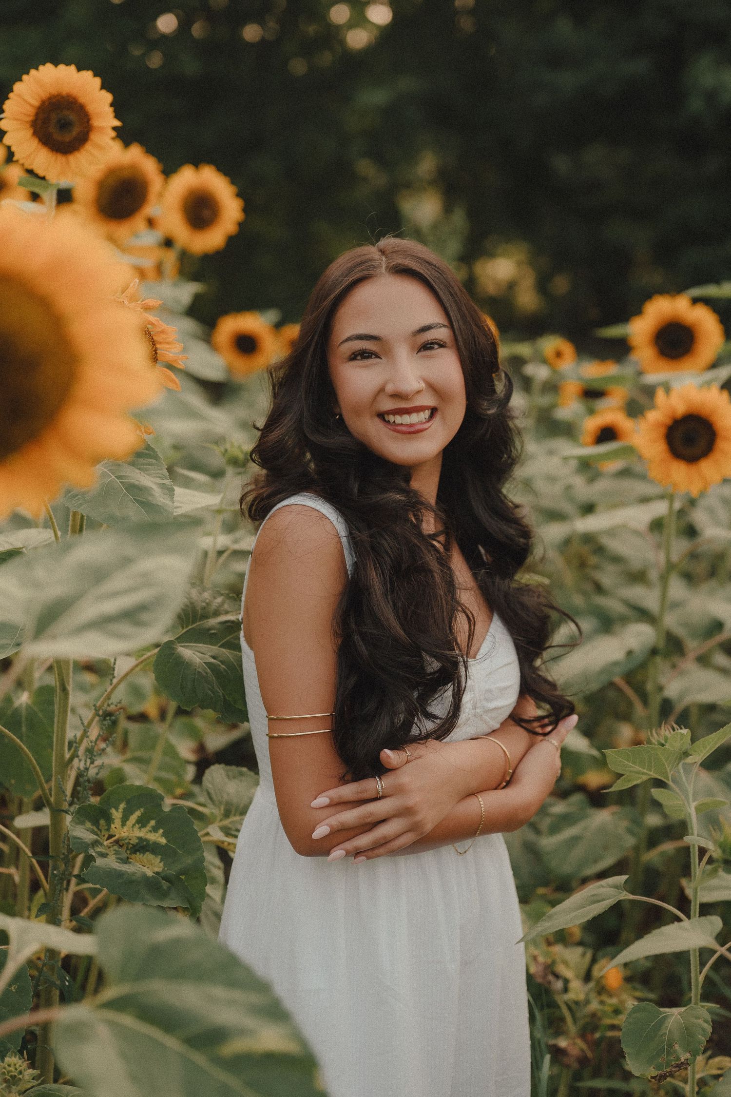 Young woman in white dress smiling among sunflowers in golden hour light.