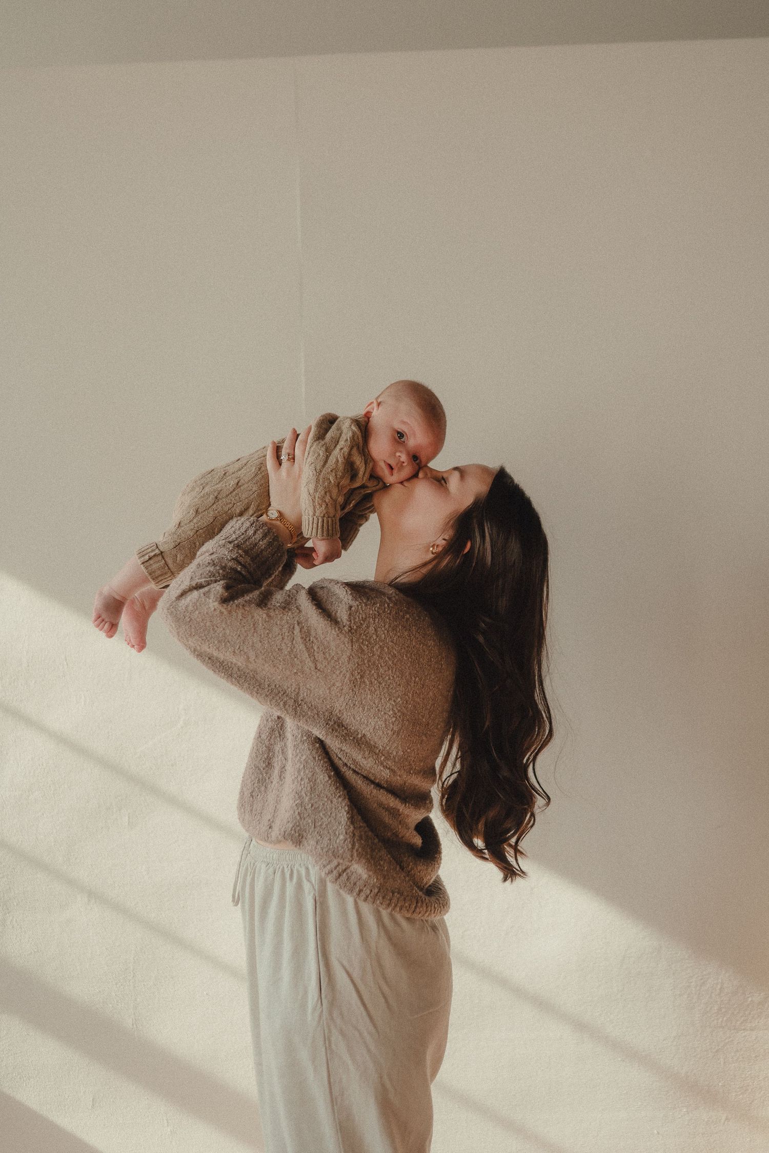 Intimate lifestyle photoshoot showing tender moments between two people in a light-filled room with neutral tones.