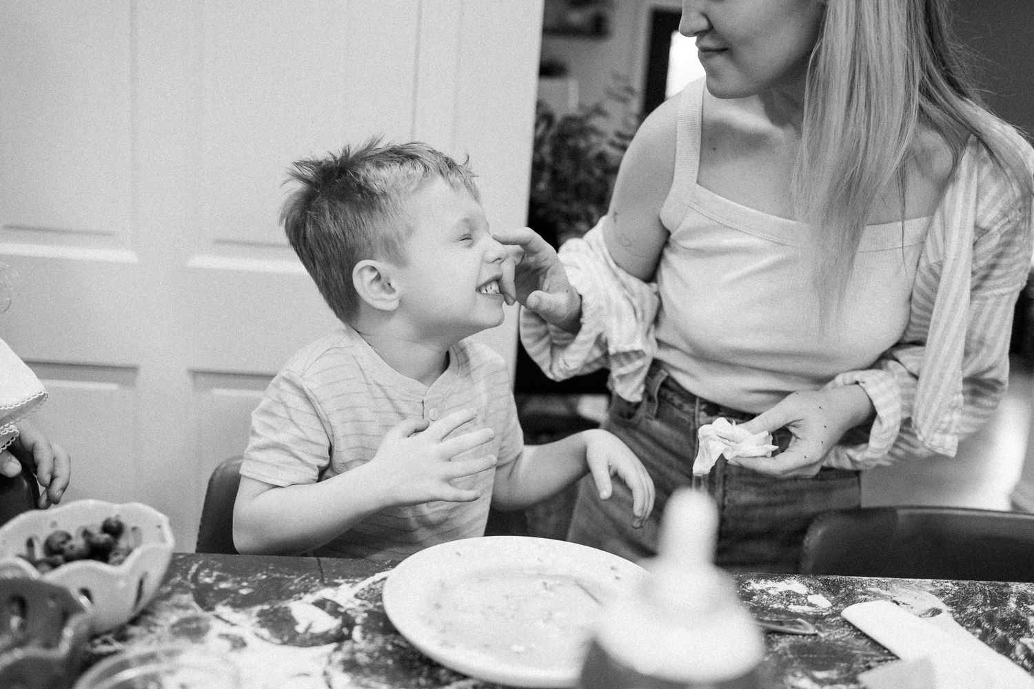 Mother feeding young son a taste while baking together at kitchen counter.