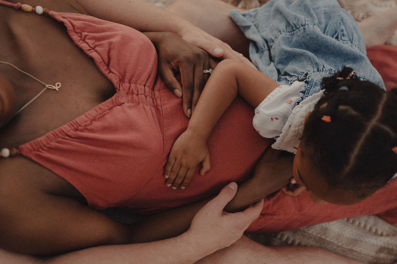 Pregnant woman lying down with young child resting on her baby bump in a tender moment.