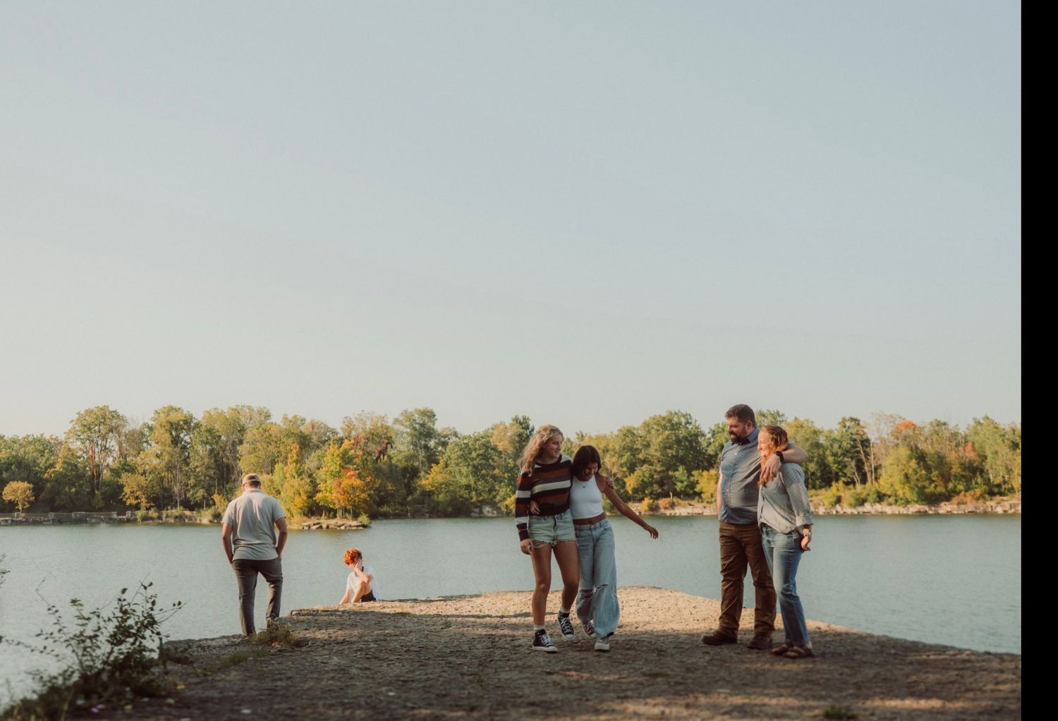 Silhouettes of people gathered along a serene lakeshore at sunset.