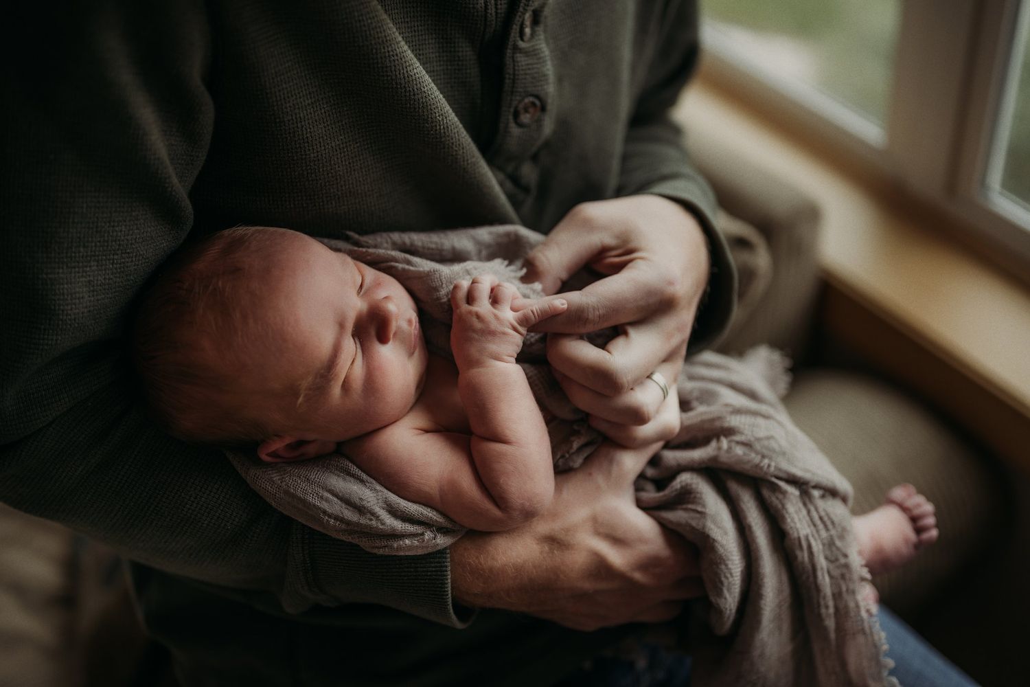 A tender moment between parent and newborn baby by a sunlit window.