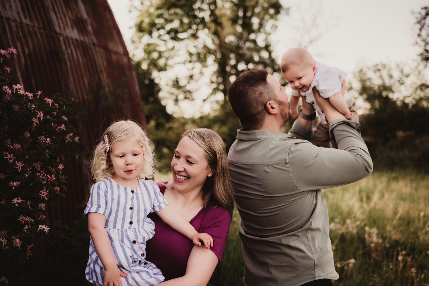 Family moment captured by rustic barn with burgundy and grey clothing details.