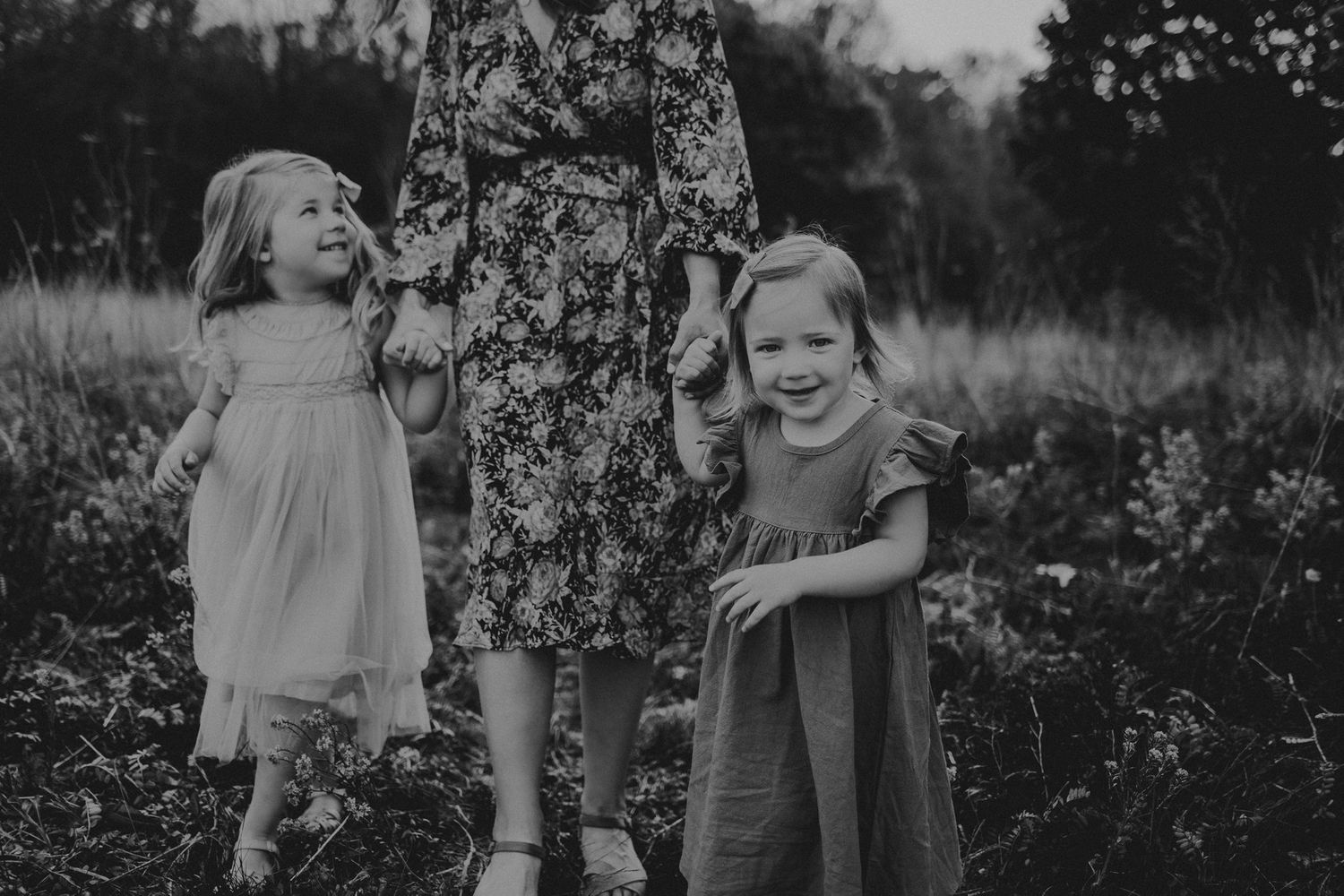 Black and white portrait of playful children in flowing dresses beside floral pattern.