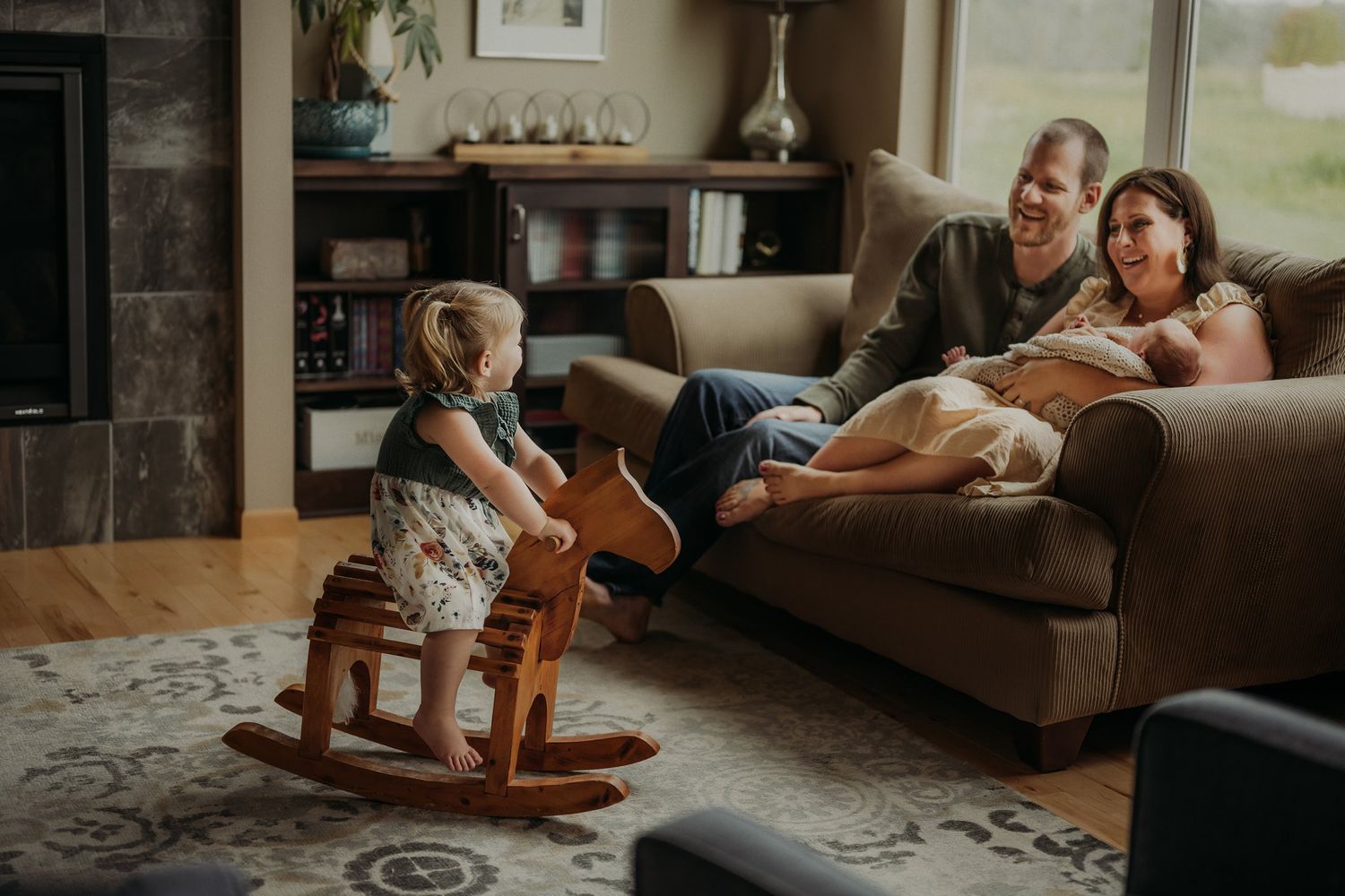 A living room scene with a child on a rocking horse while others rest on a brown couch.