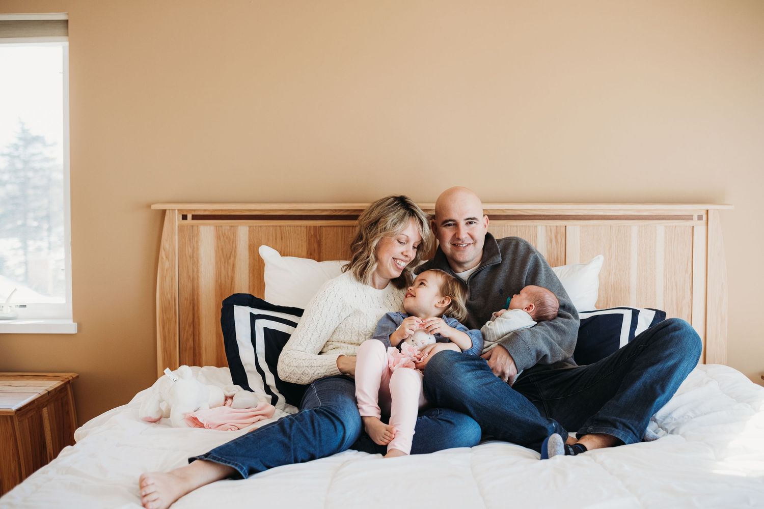 A family shares a tender moment together while relaxing on a bed with white bedding.
