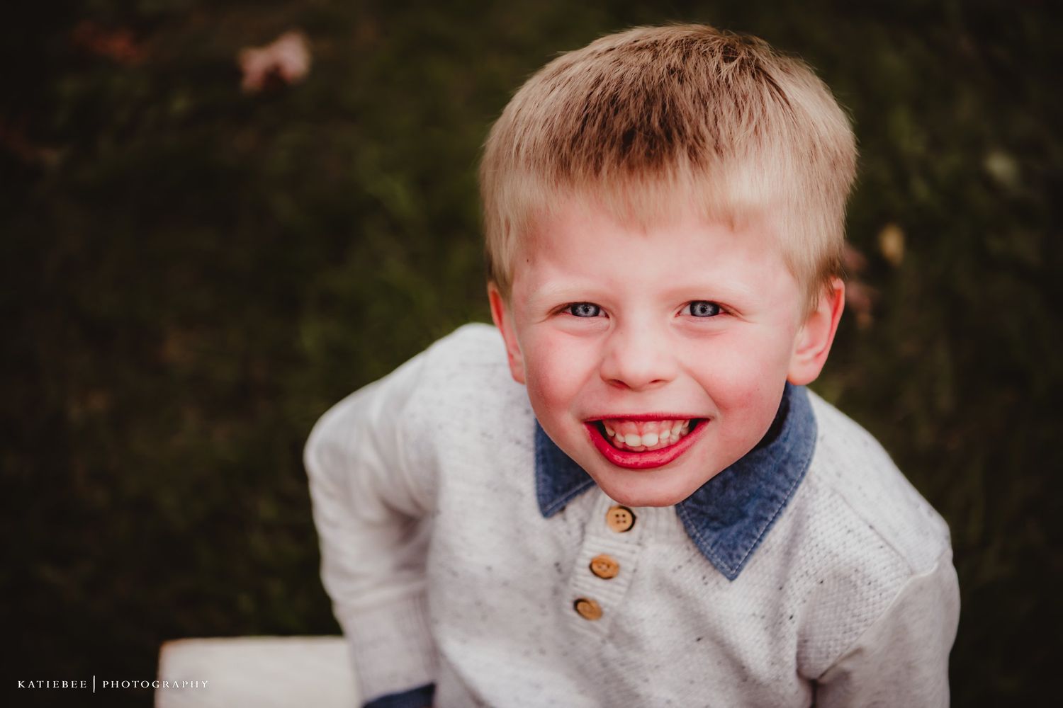 Close up portrait of a smiling child wearing a cream colored sweater with button details.