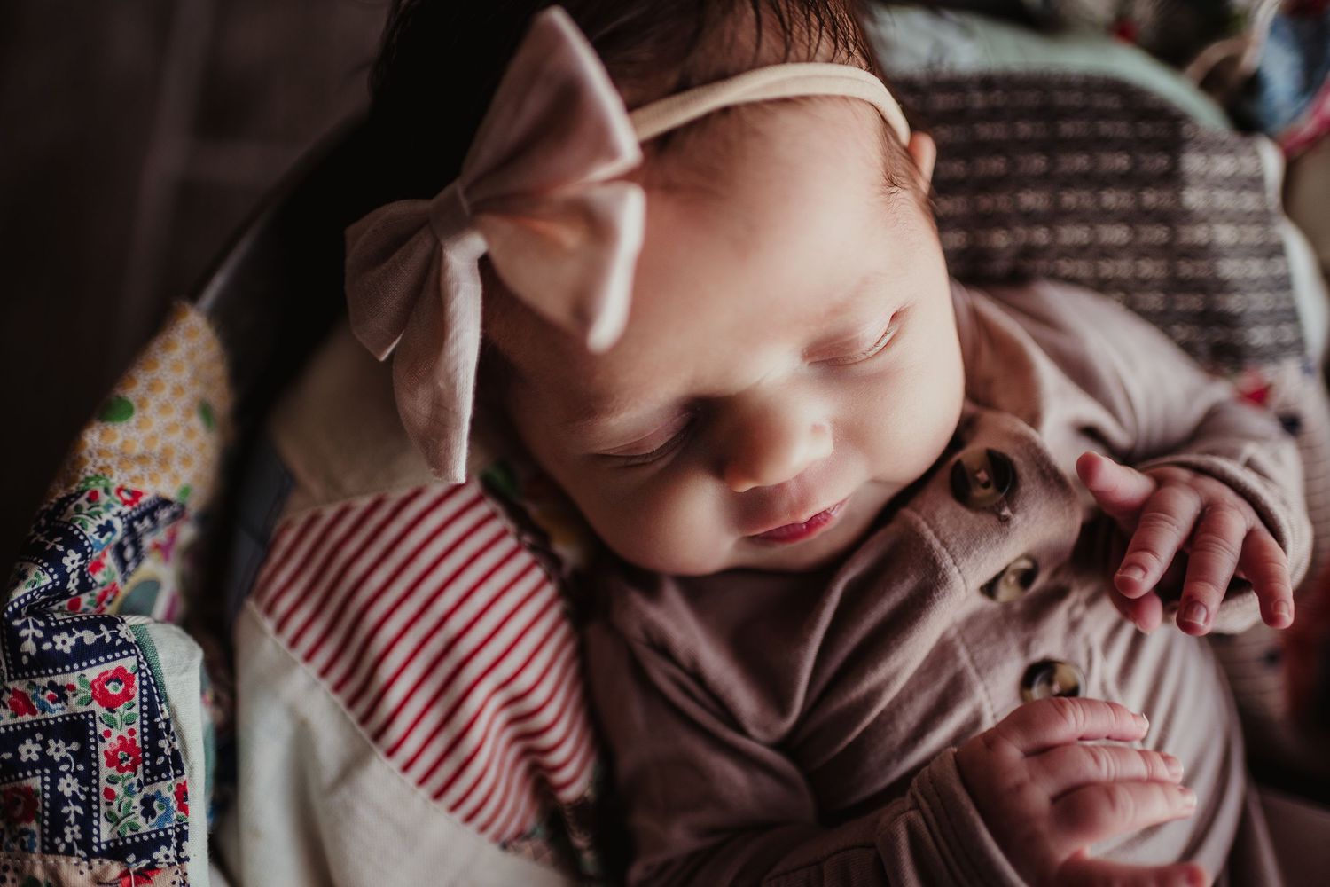 Sleeping baby wearing pink bow headband in cozy floral outfit.