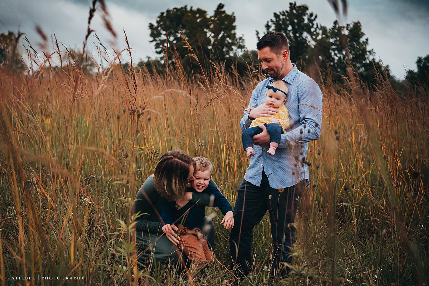 Family enjoying a playful moment together in a field of tall grass at sunset.