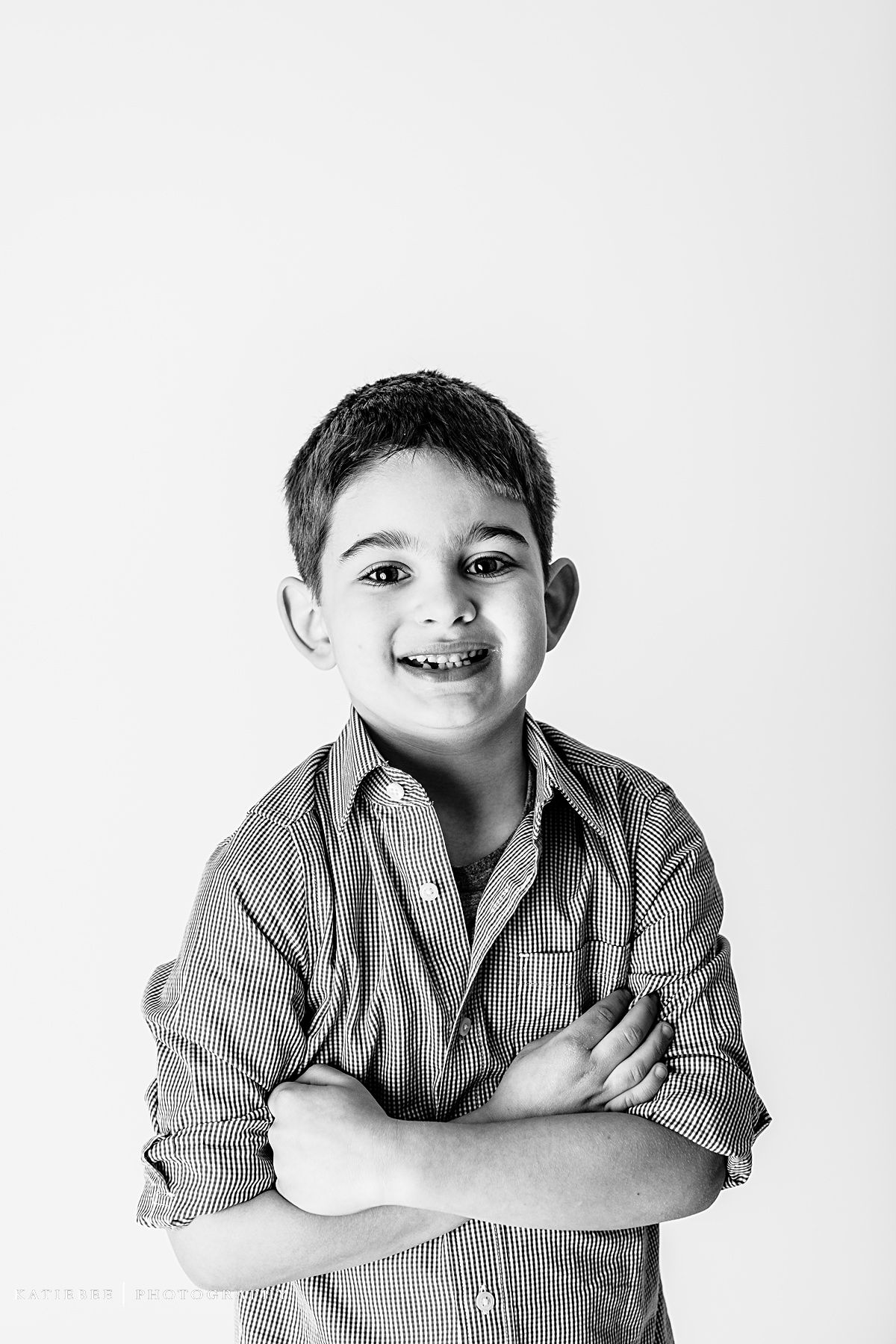Child in striped button-down shirt posing with crossed arms in black and white studio shot.