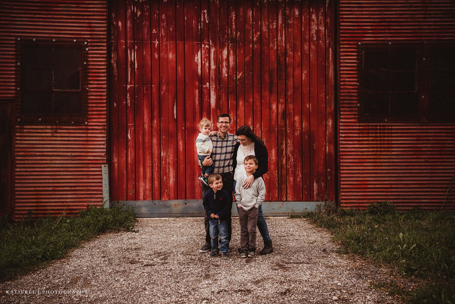 Two people standing in front of large red barn doors during photo session.