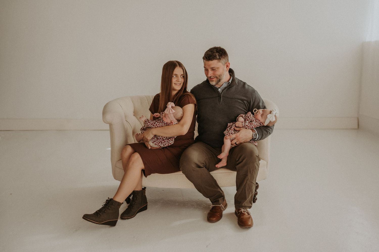 Parents and twin babies share intimate family moment on vintage sofa in bright studio setting.