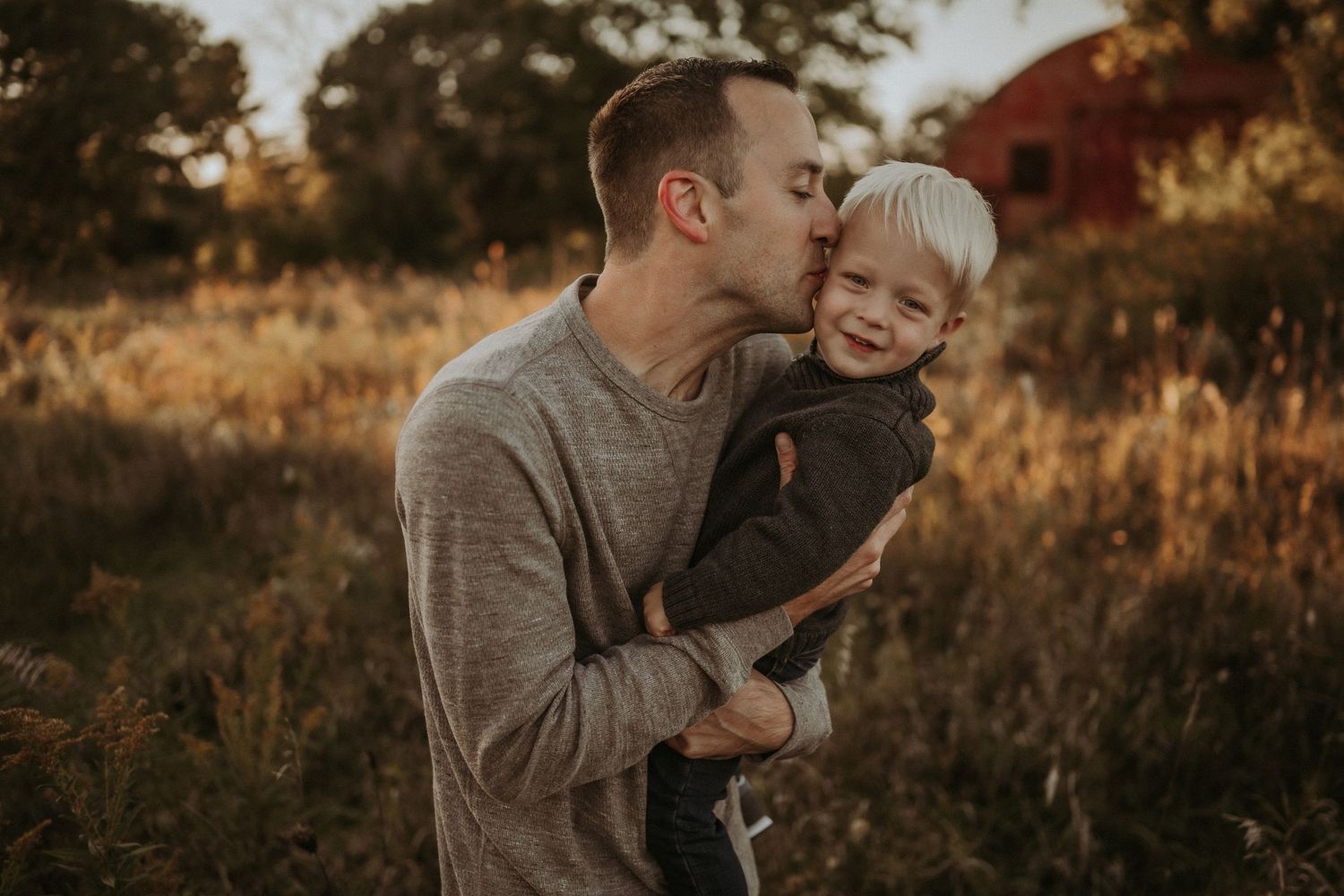 Sweet embrace shared between parent and child during sunset with rustic barn in background.