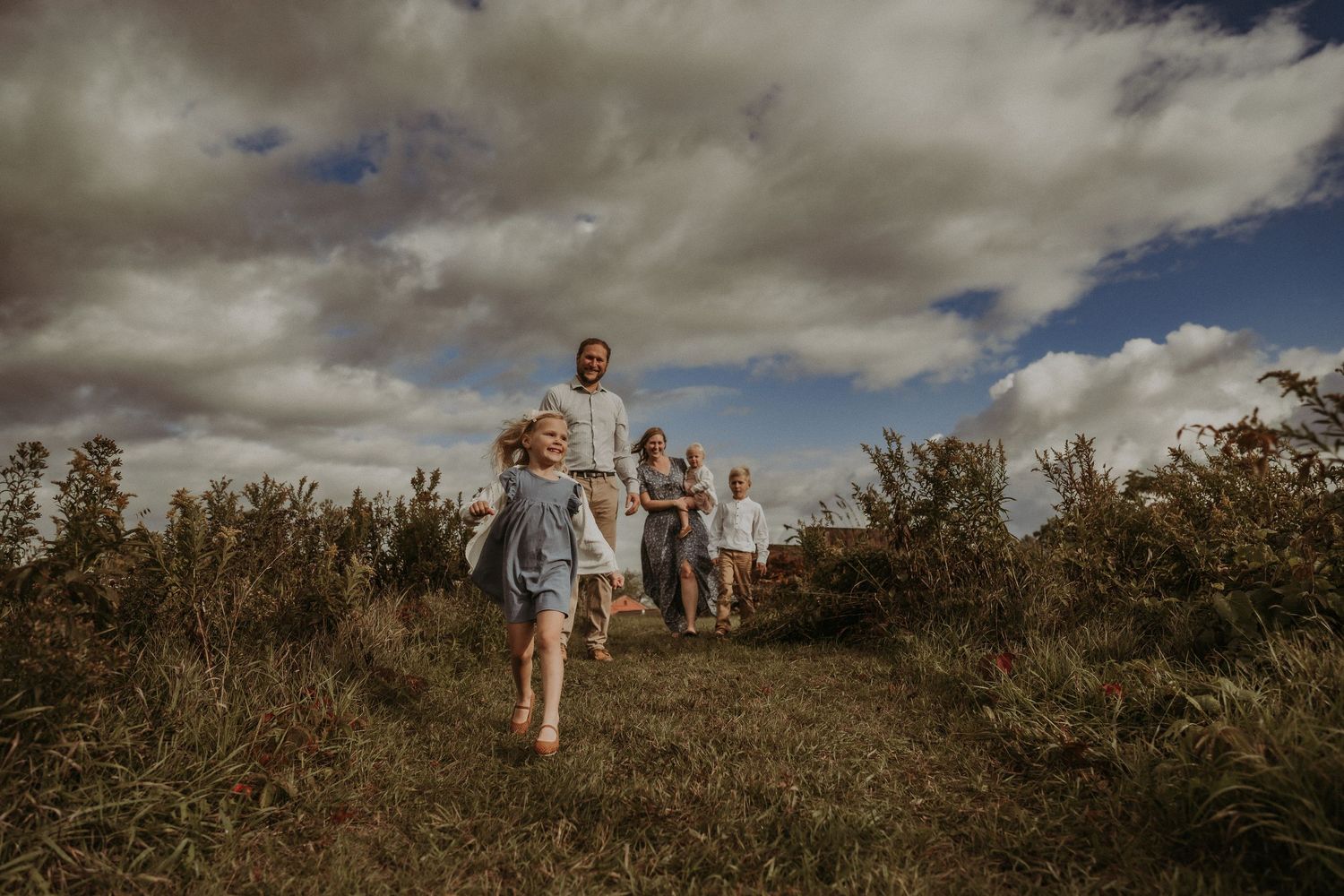 Family running together on grassy hill under dramatic cloudy sky.