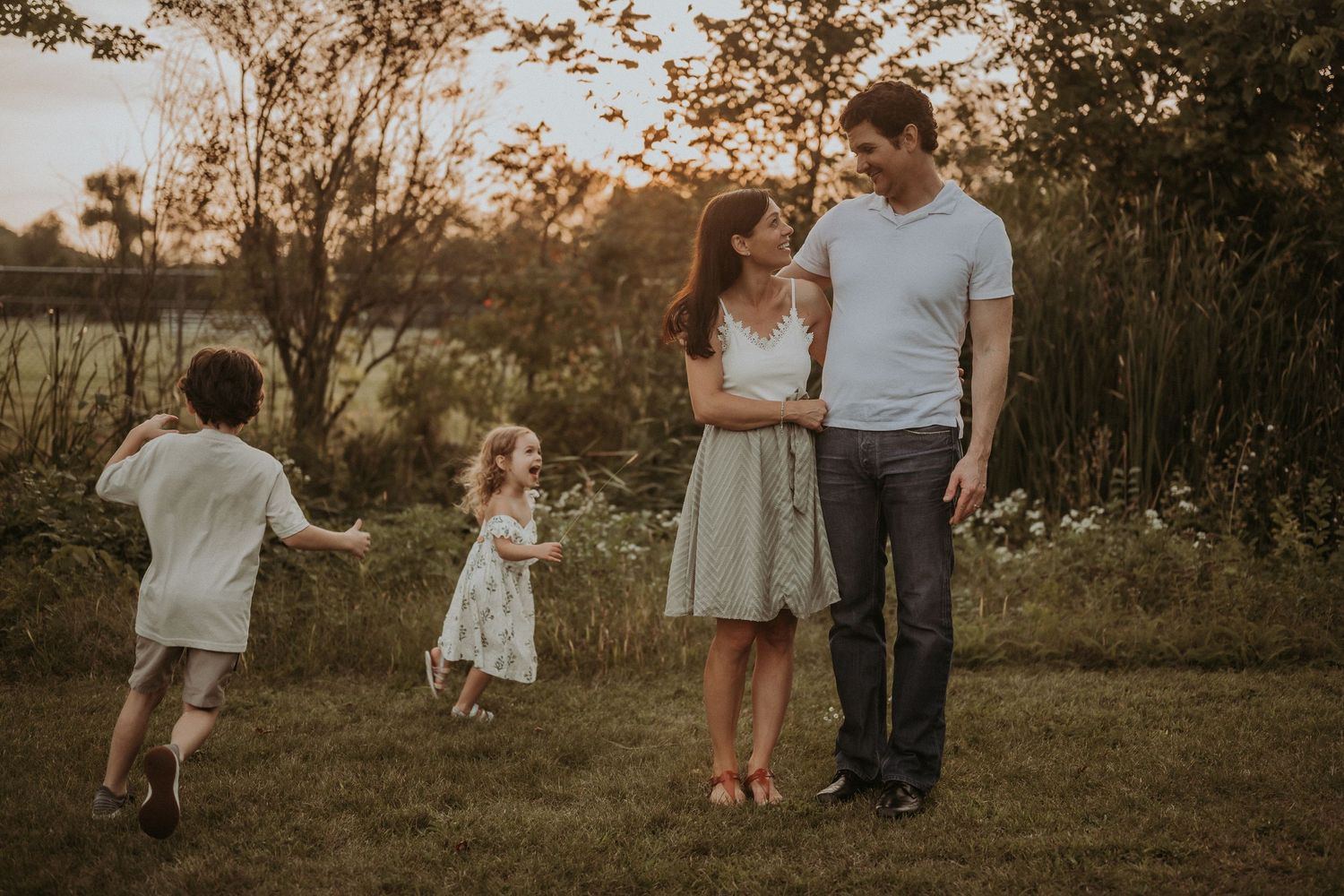 Children playing while parents watch in a golden-lit field at sunset.