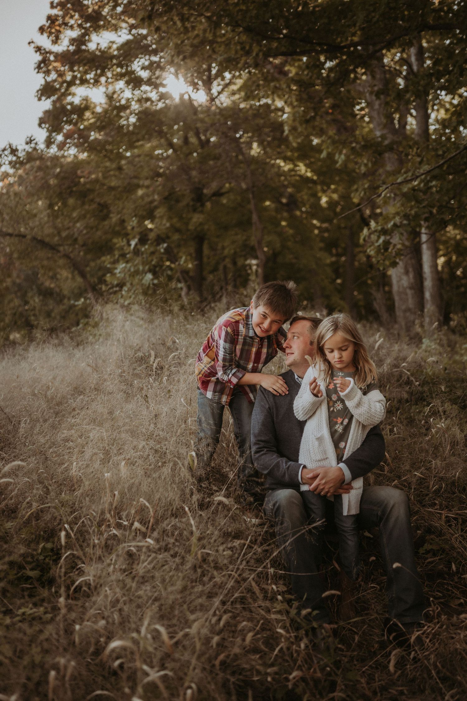 Candid family moment captured in tall grass during autumn sunset.