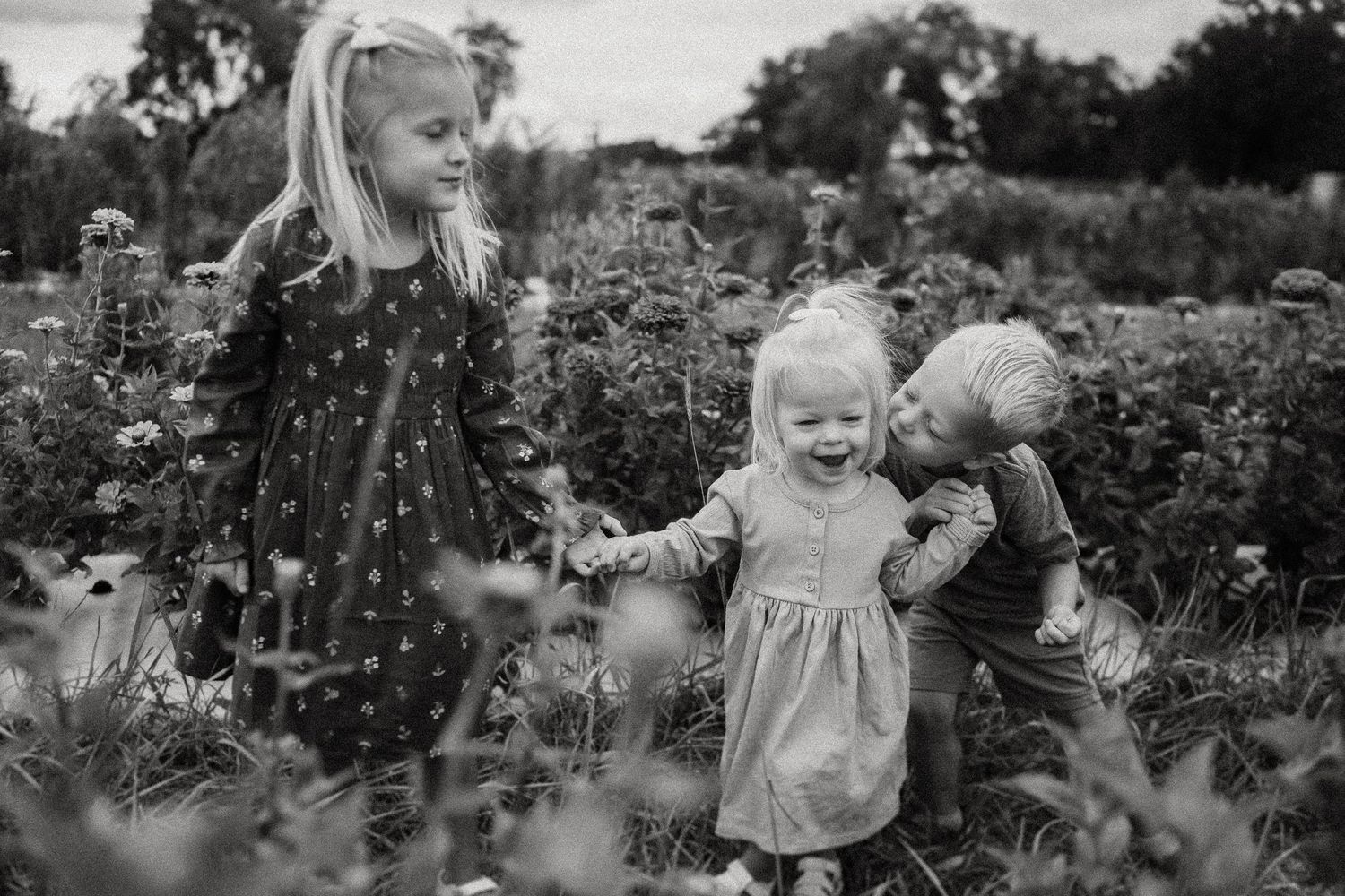 Young children exploring together in a blooming garden filled with flowers.