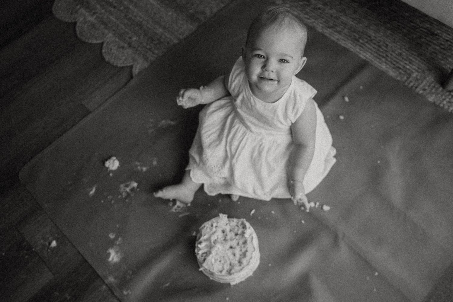 Black and white high-angle view of a messy cake smash photo session on a dark surface.