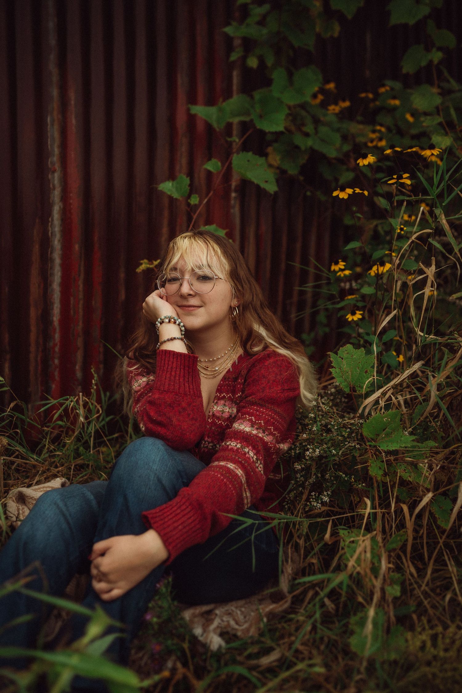 A casual outdoor portrait by a red barn wall surrounded by autumn wildflowers and greenery.