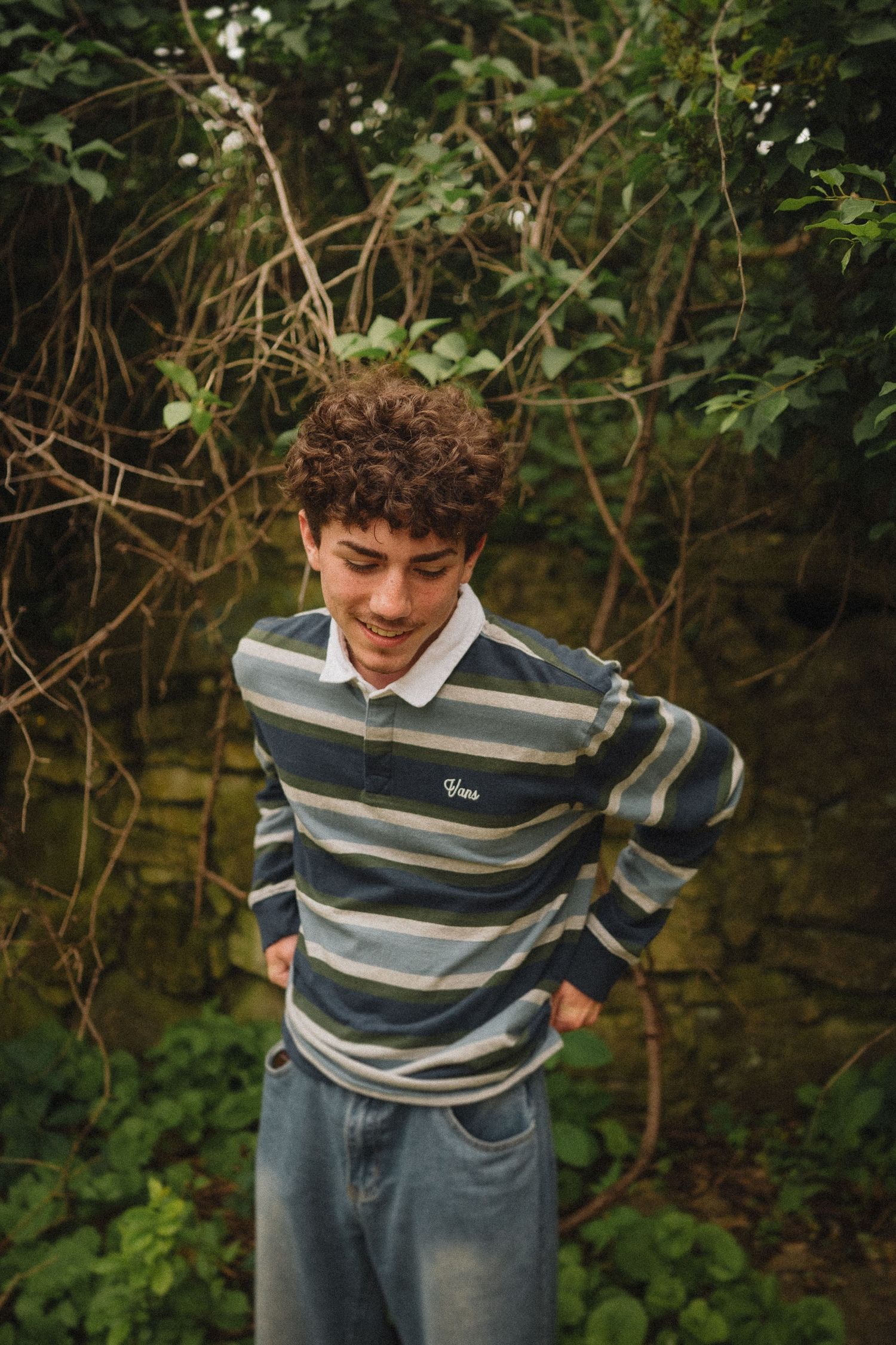 Candid outdoor photo of someone wearing a striped rugby shirt and jeans in a garden setting.